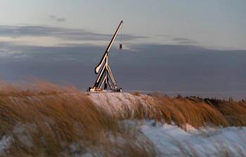 Skagen om vinteren med en dramatisk kranstruktur på snedækkede klitter omgivet af gyldent strandgræs og en pastelfarvet vinterhimmel ved solopgang
