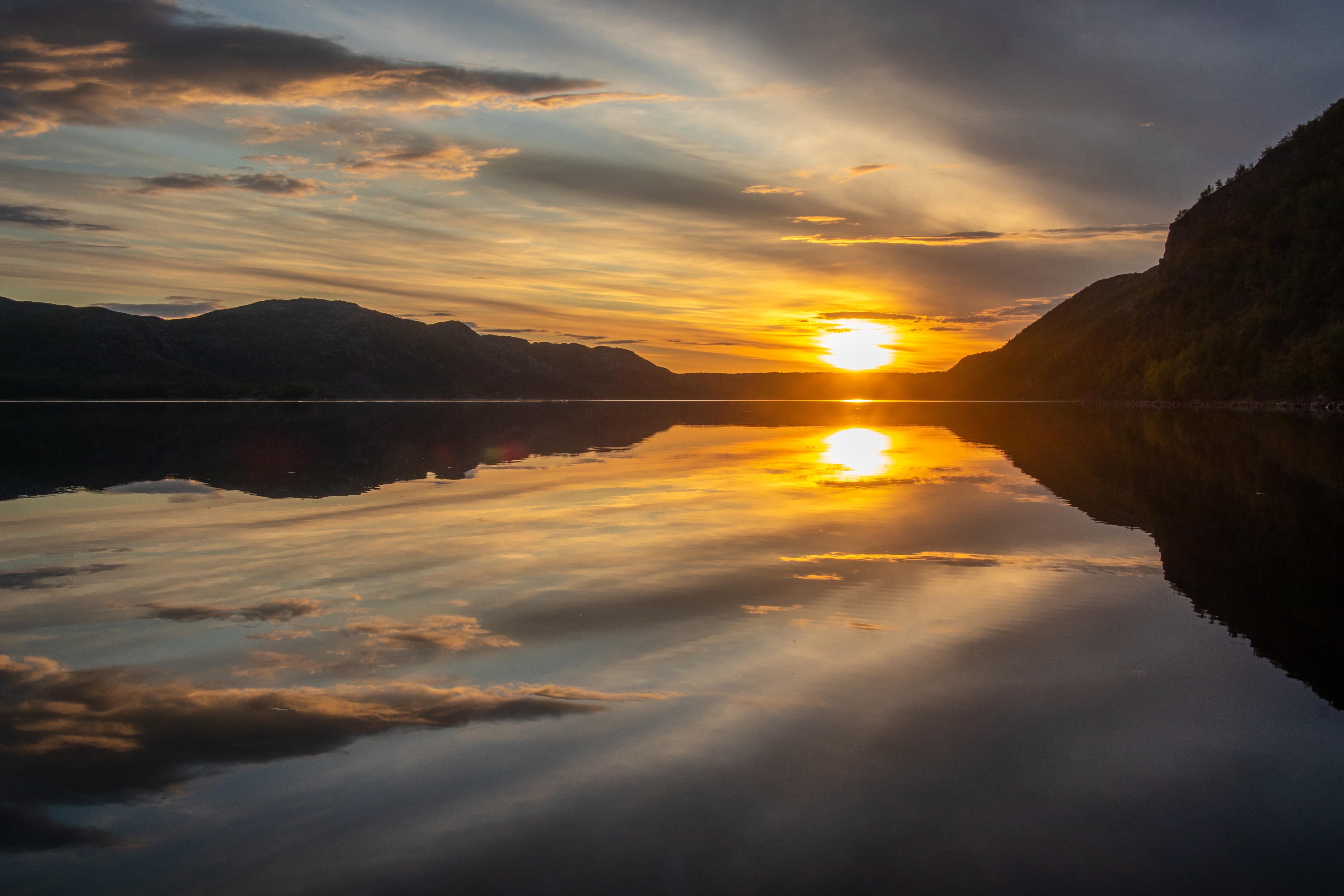 Drømmeagtig solnedgang ved skandinavisk bjergsø med guldfarvet himmel og stille vand