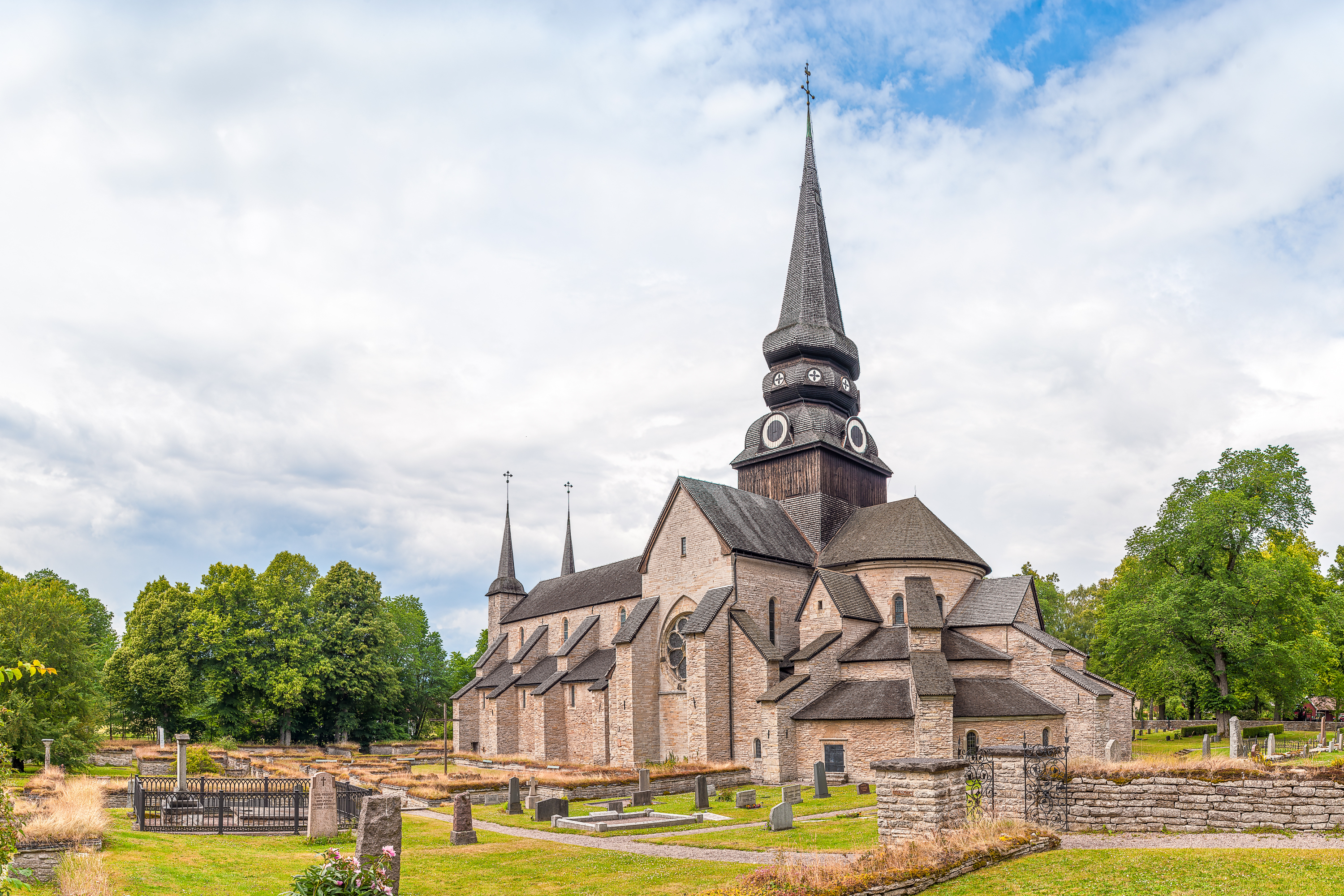 Smuk middelalderlig stenkirke med højt spir i pittoresk svensk landskab med træer