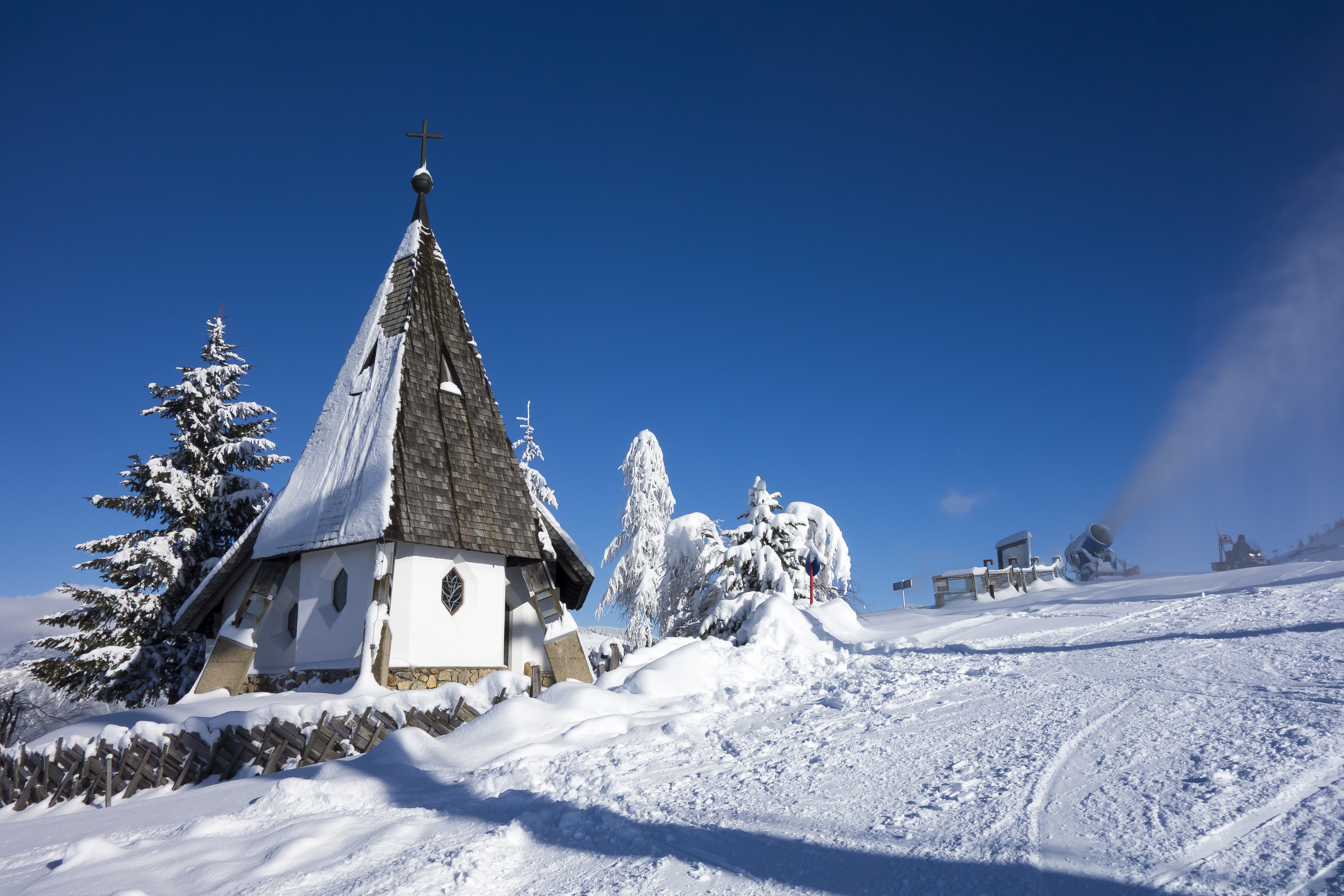 Idyllisk alpinekirke i dyb sne med træspir blandt rimfrostdækkede nåletræer på vinterferiested i bjergene