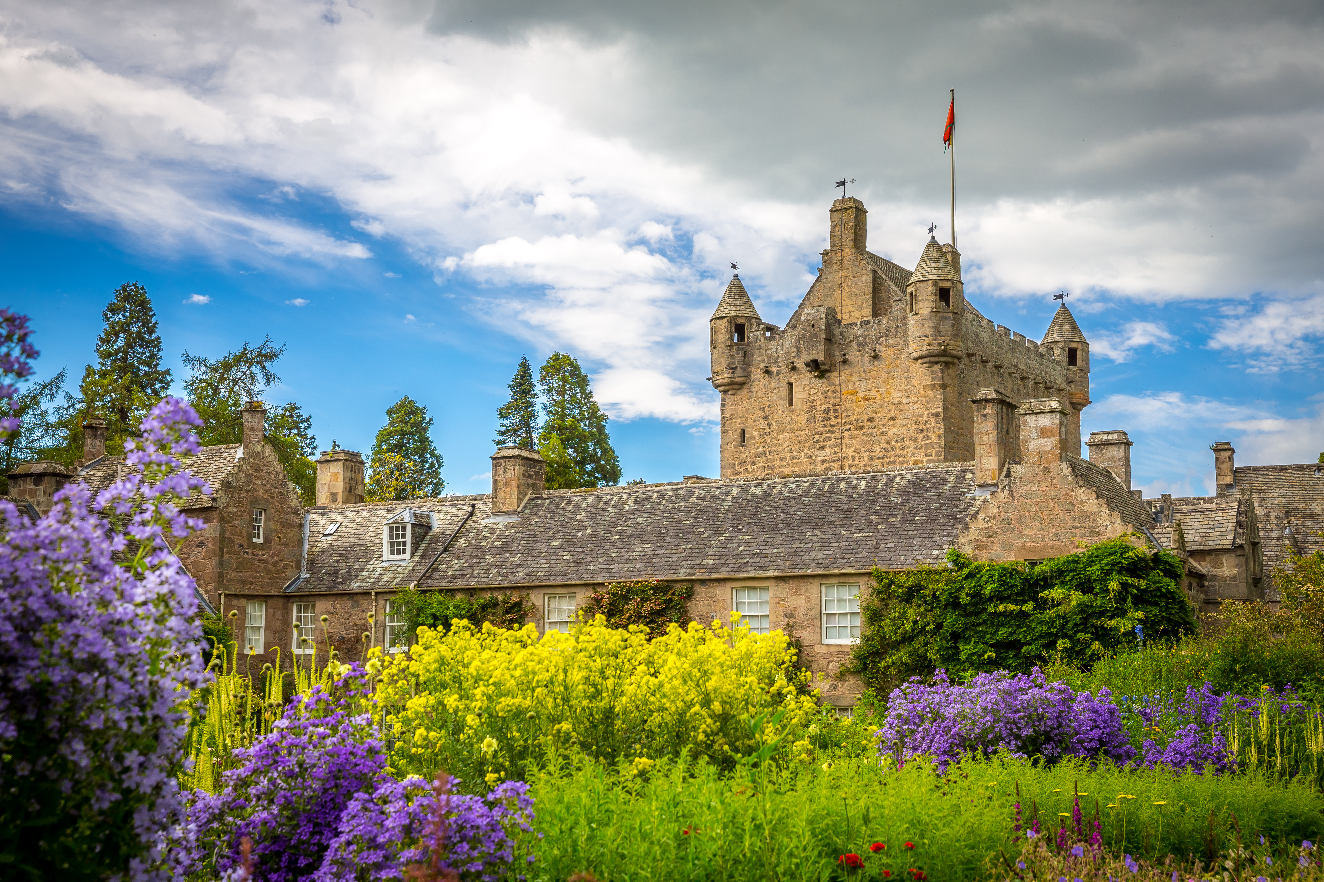 Cawdor Castle omgivet af pragtfulde blomsterhaver i de skotske højlande med lilla blomster og gul raps i forgrunden