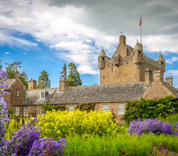 Cawdor Castle omgivet af pragtfulde blomsterhaver i de skotske højlande med lilla blomster og gul raps i forgrunden