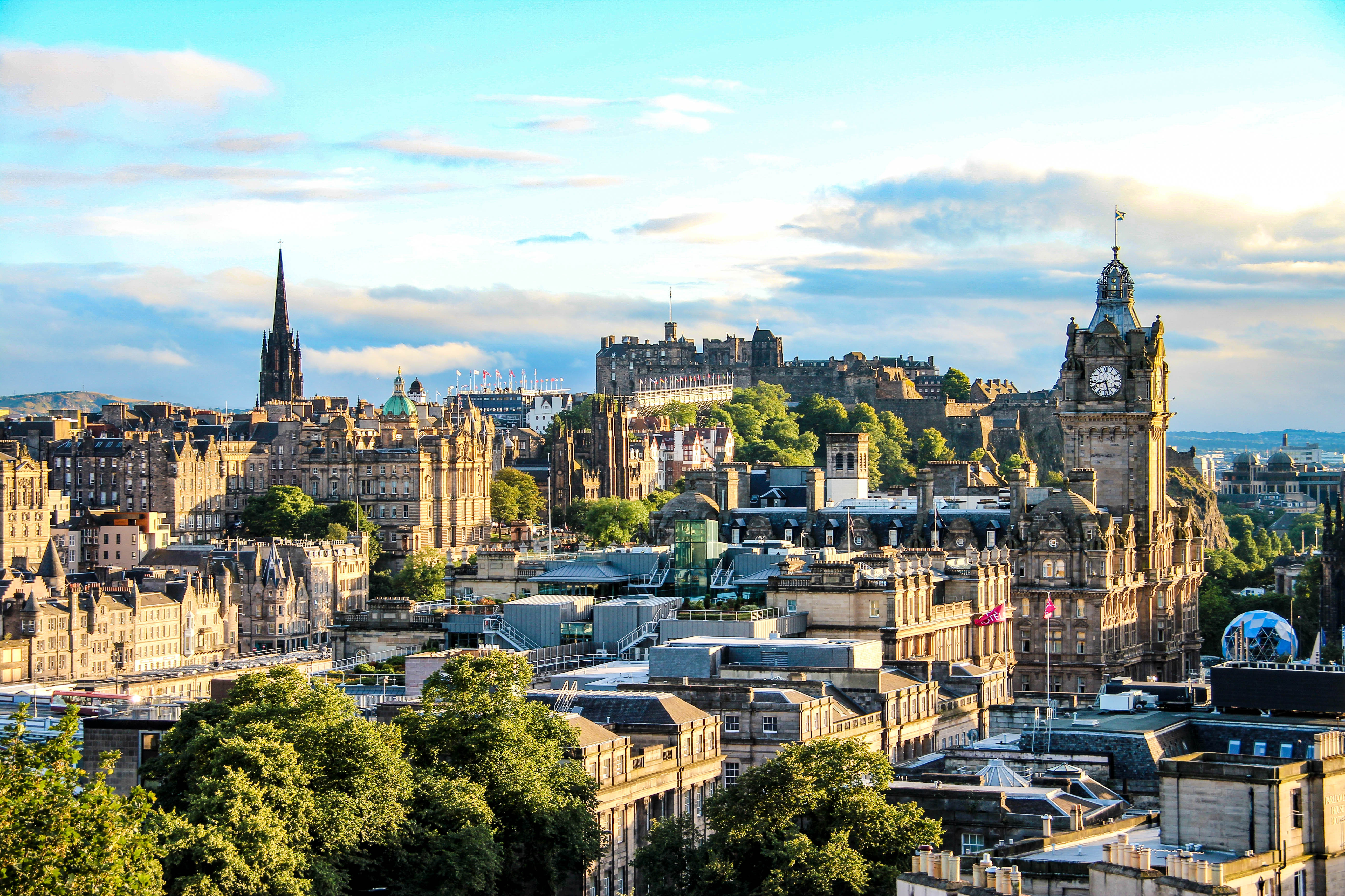 Fantastisk bylandskab over Edinburgh med traditionel skotsk arkitektur, kirketårne og det majestætiske slot badet i varmt eftermiddagslys
