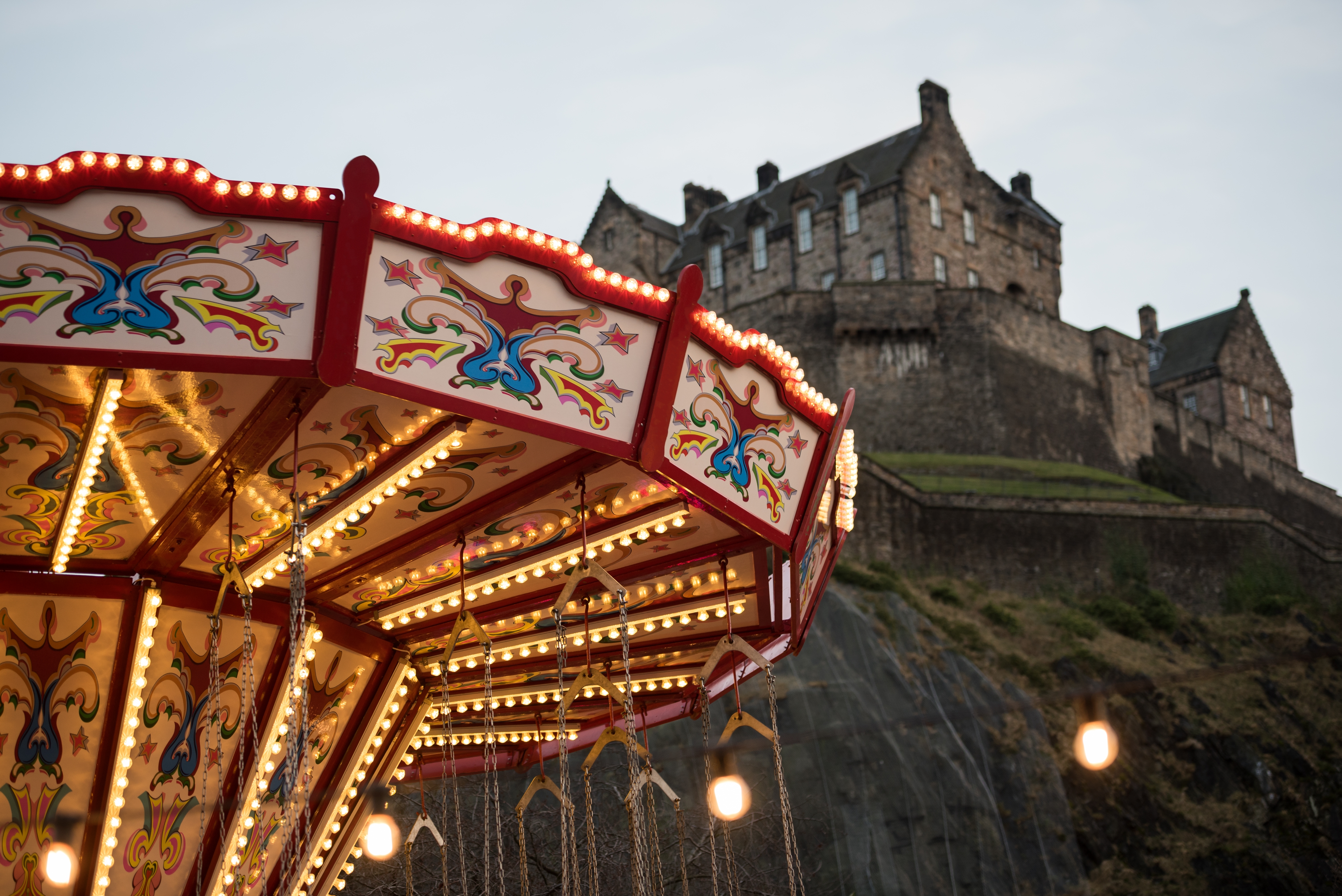 Klassisk oplyst karrusel med gynger ved Edinburgh julemarked med udsigt til det historiske Edinburgh Castle på klippetoppen