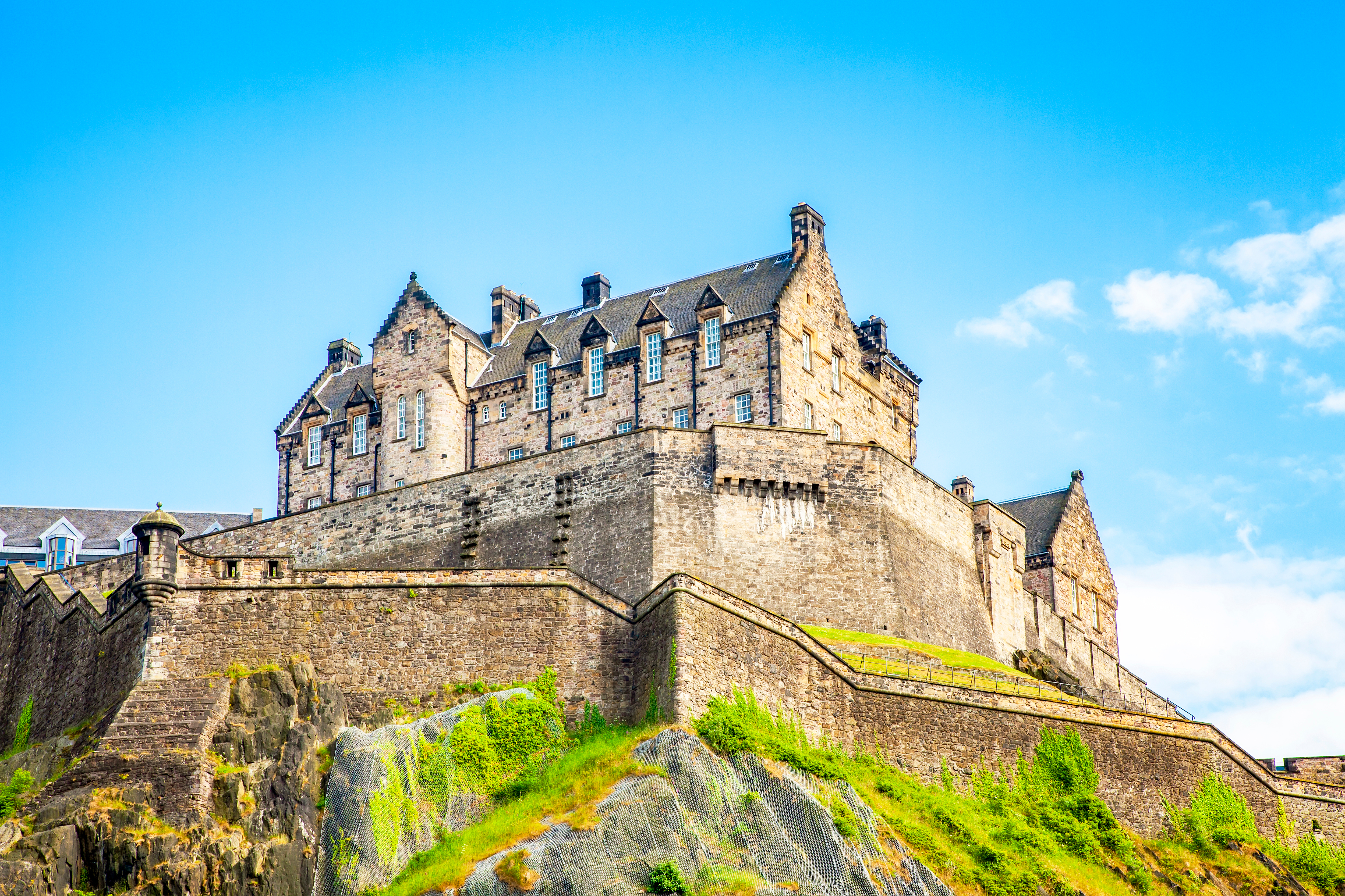 Magtfuldt Edinburgh slot på høj klippe omgivet af grøn vegetation under sommerhimmel