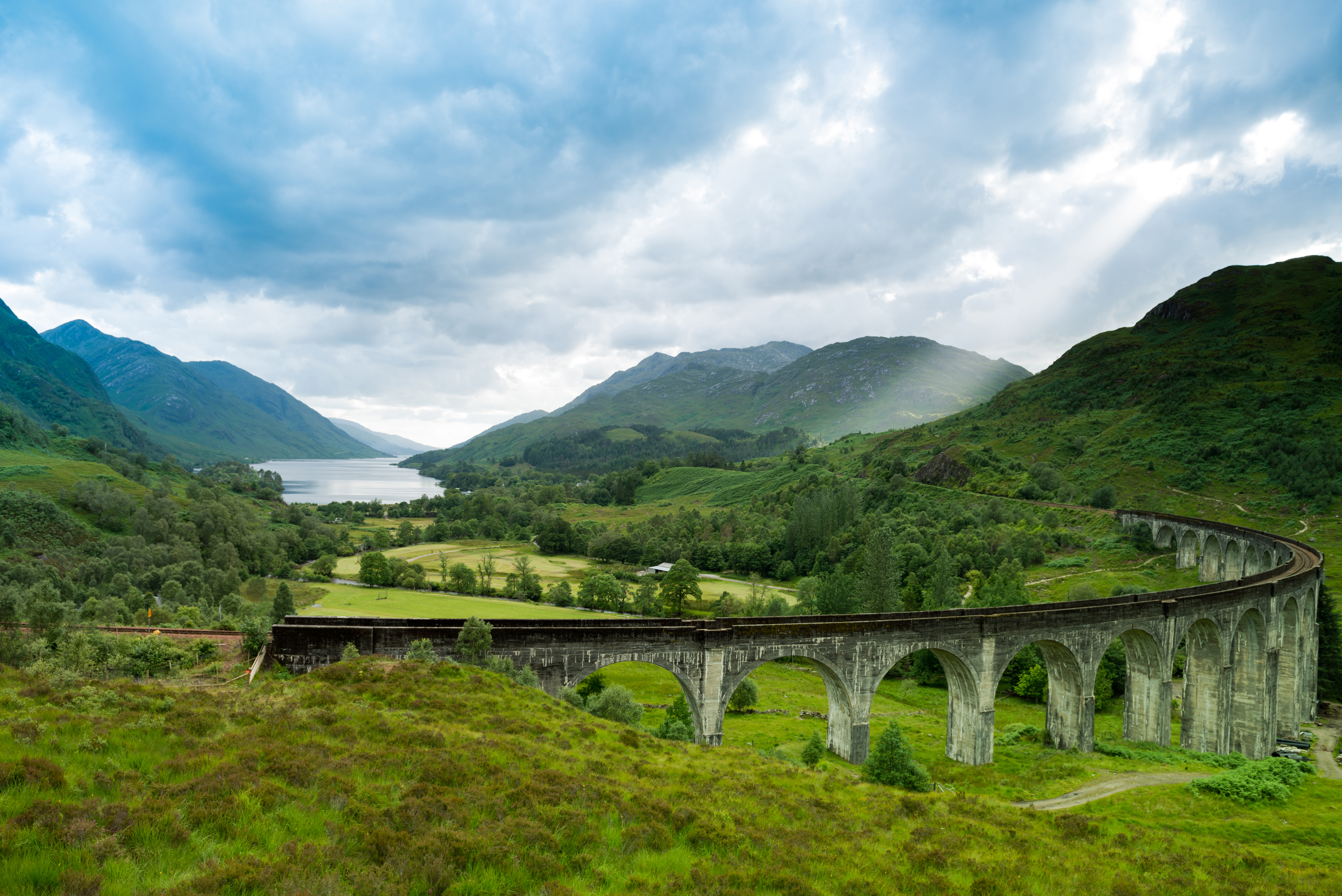 Glenfinnan Viadukt i Skotlands smukke højlande med grønne bjerge og Loch Shiel i det fjerne