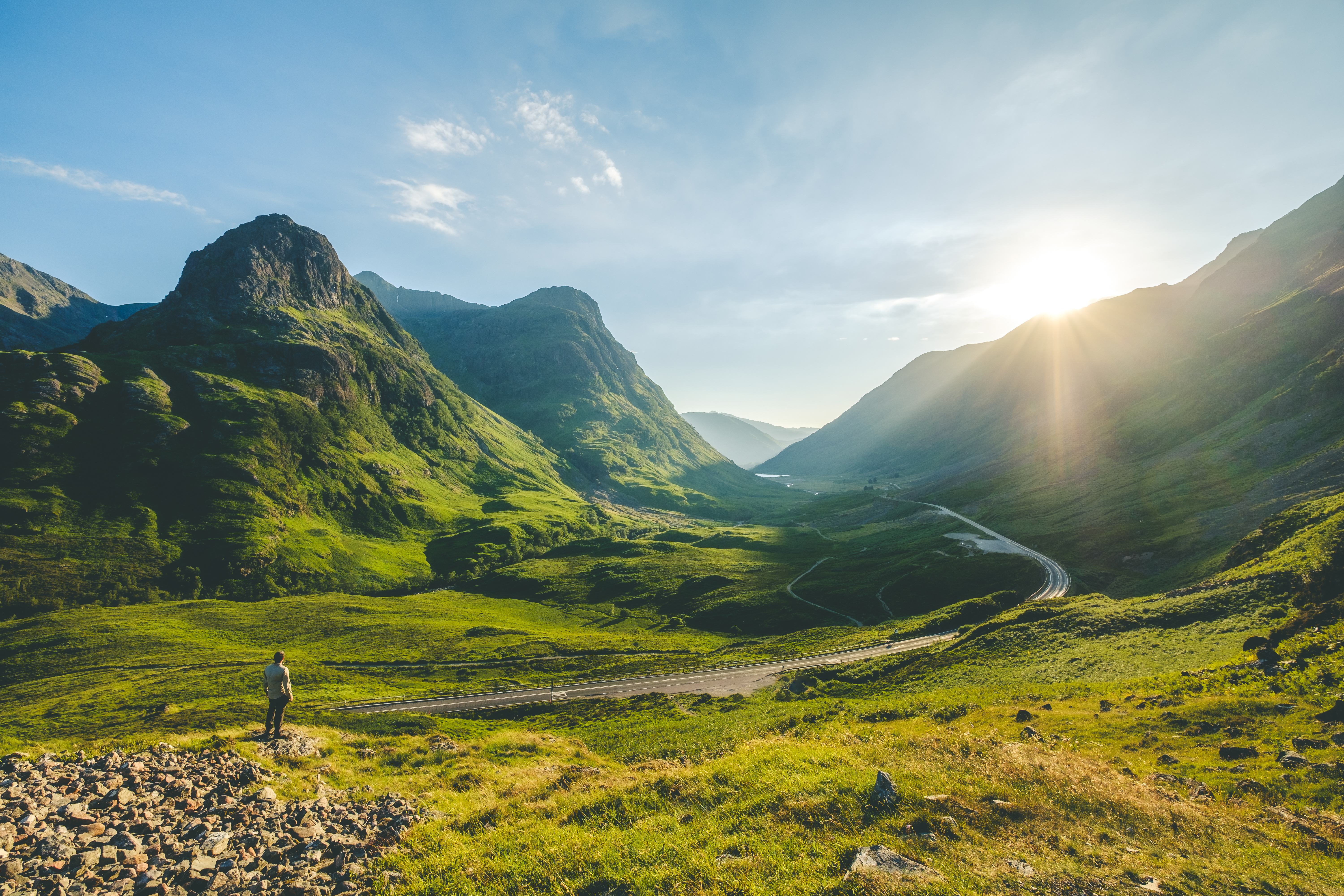 Vandrer oplever den storslåede natur i Glen Coe dalen i det skotske højland med snoet vej og gyldent sollys