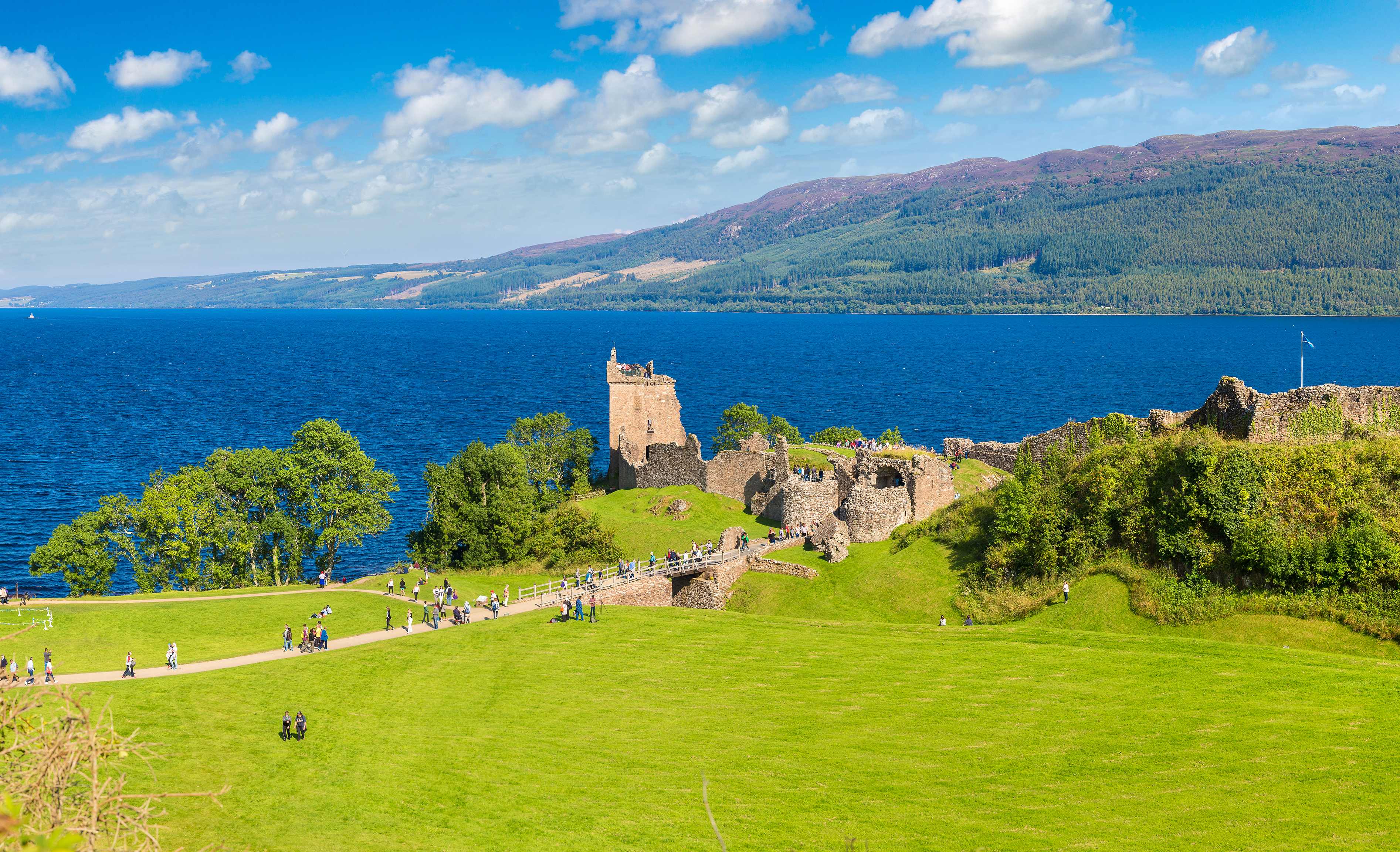 Middelalderlige ruiner af Urquhart Castle ved Loch Ness i Skotland med grønne bakker og blå himmel