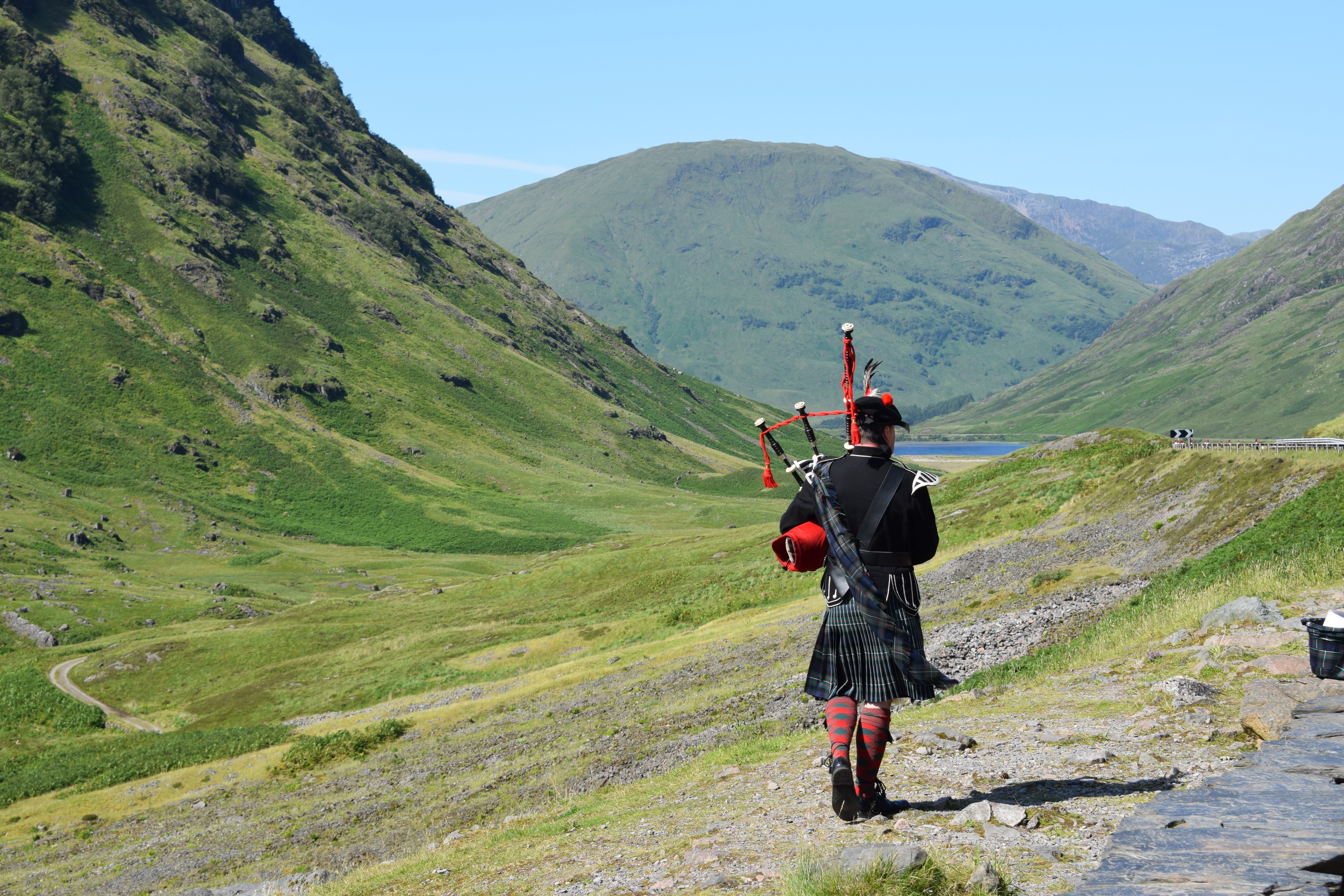 Mand i traditionelt skotsk kilt spiller sækkepibe i de storslåede grønne highlands i Skotland