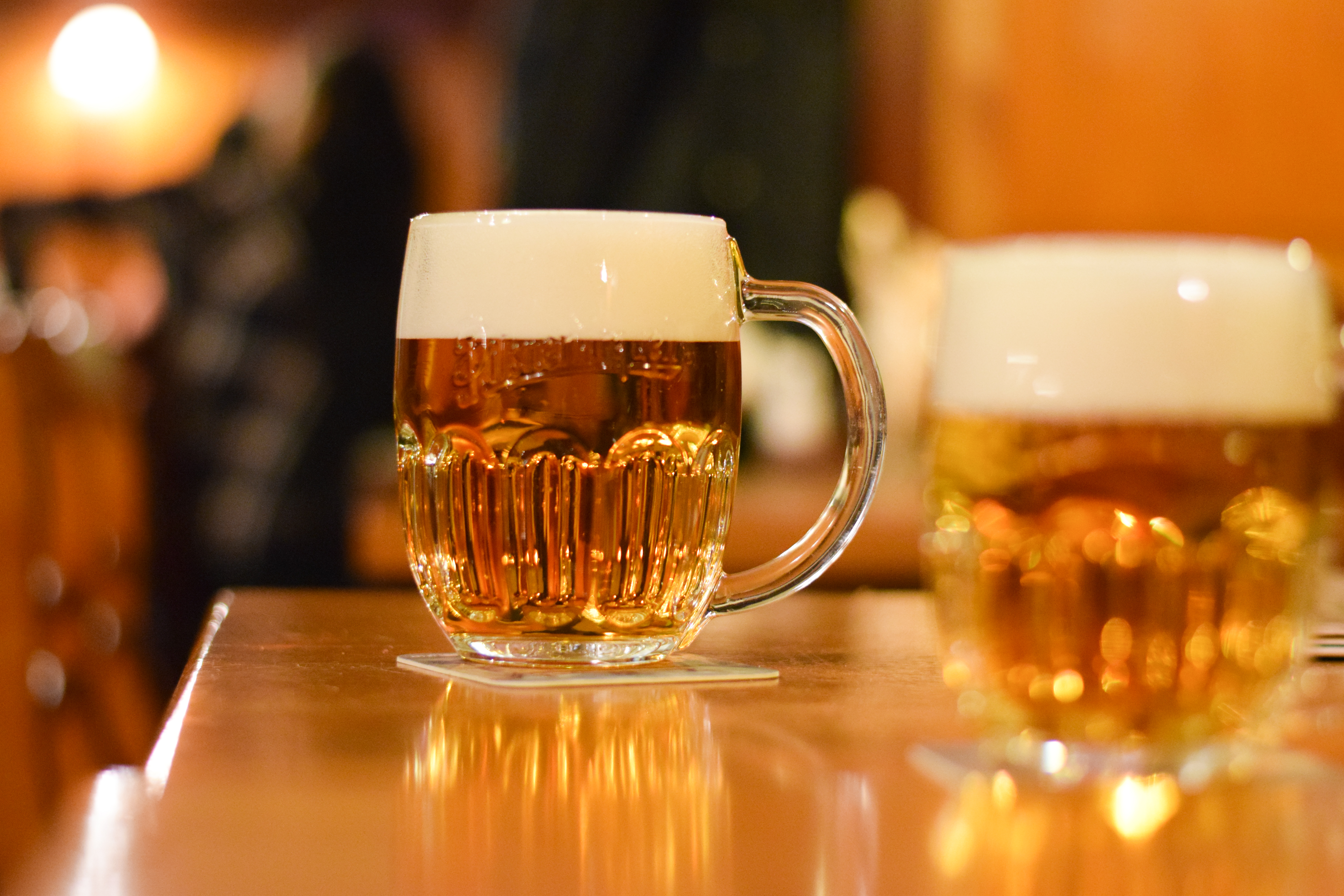 Skummende øl i klassisk krus på træbord med varm belysning i autentisk pub