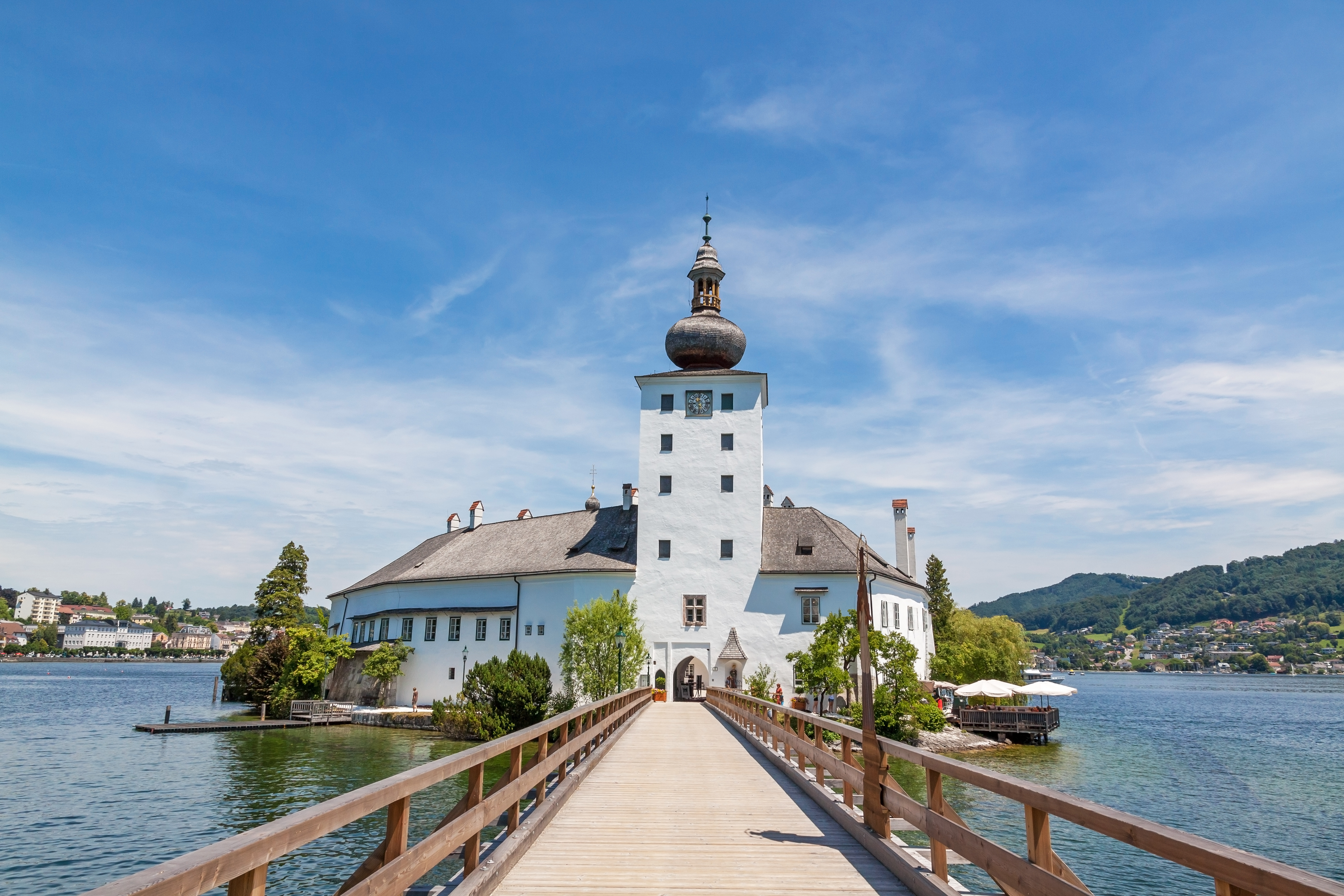 Idyllisk Schloss Ort vandslot ved Traunsee i Gmunden, Østrig, med lang træbro og blå sommerhimmel