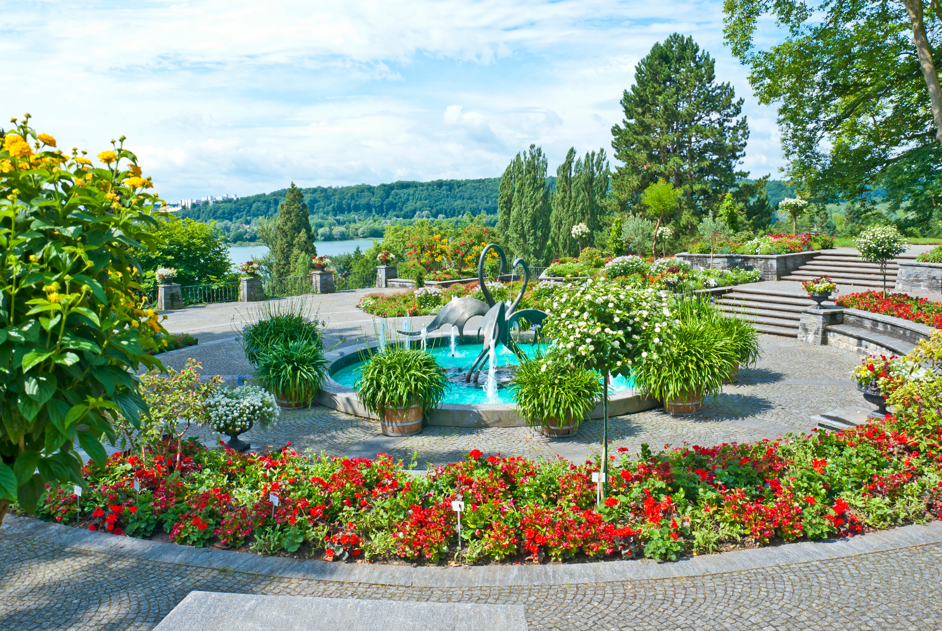 Fredelig søhave med kunstnerisk fontæne og farvestrålende blomster på stenlagt terrasse