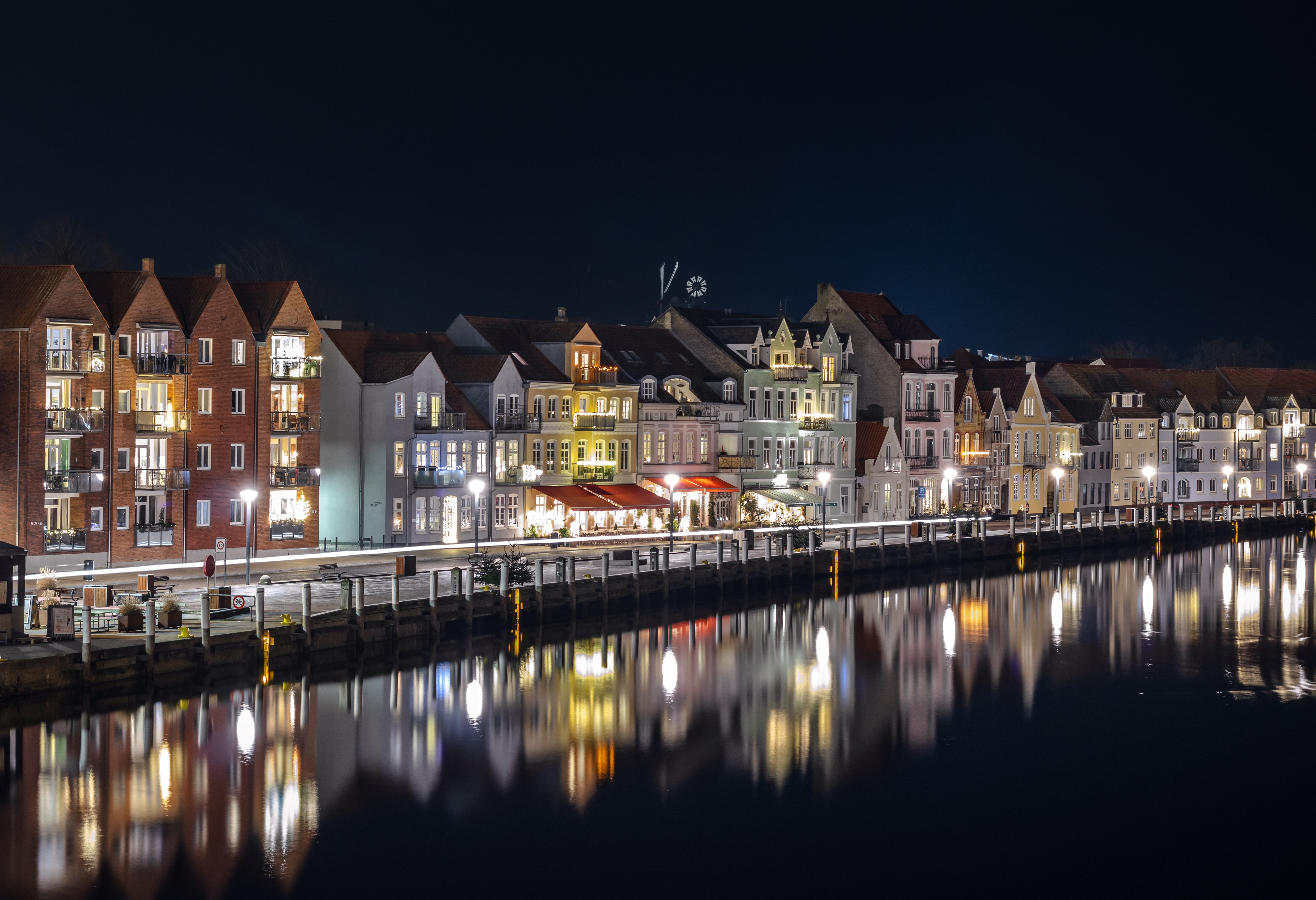 Idyllisk aftenstemning ved Sønderborg Havn før jul, hvor byens lys spejler sig i det mørke vand og skaber en eventyrlig atmosfære langs den sønderjyske kystlinje