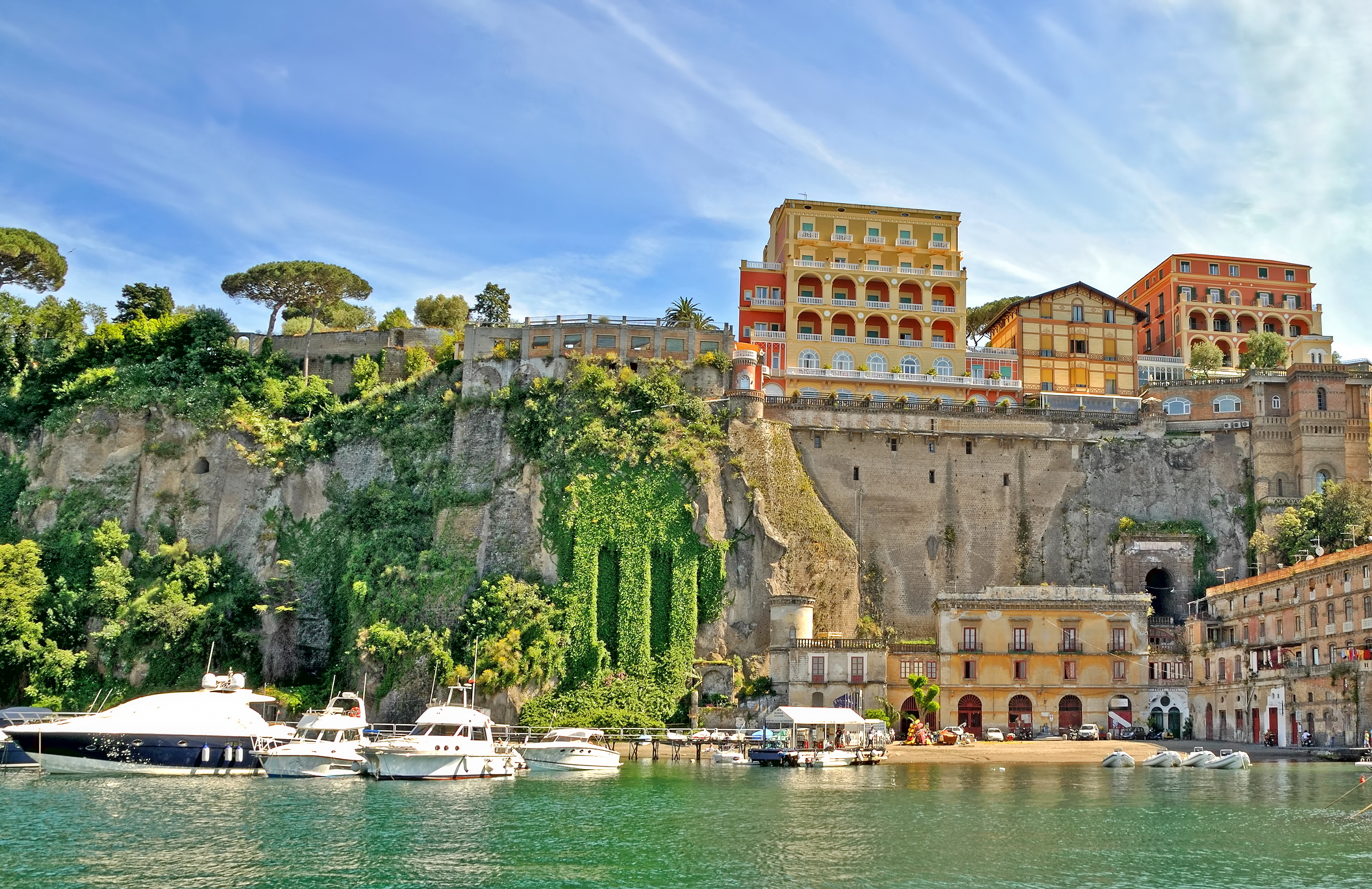 Charmerende udsigt over Sorrentos havnefront med historiske bygninger på de stejle klipper og farverige både i det blå Middelhav i Syditalien