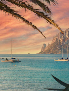 Malerisk spansk kyst med sejlbåde og dramatisk Es Vedra klippeformation ved solnedgang, Ibiza
