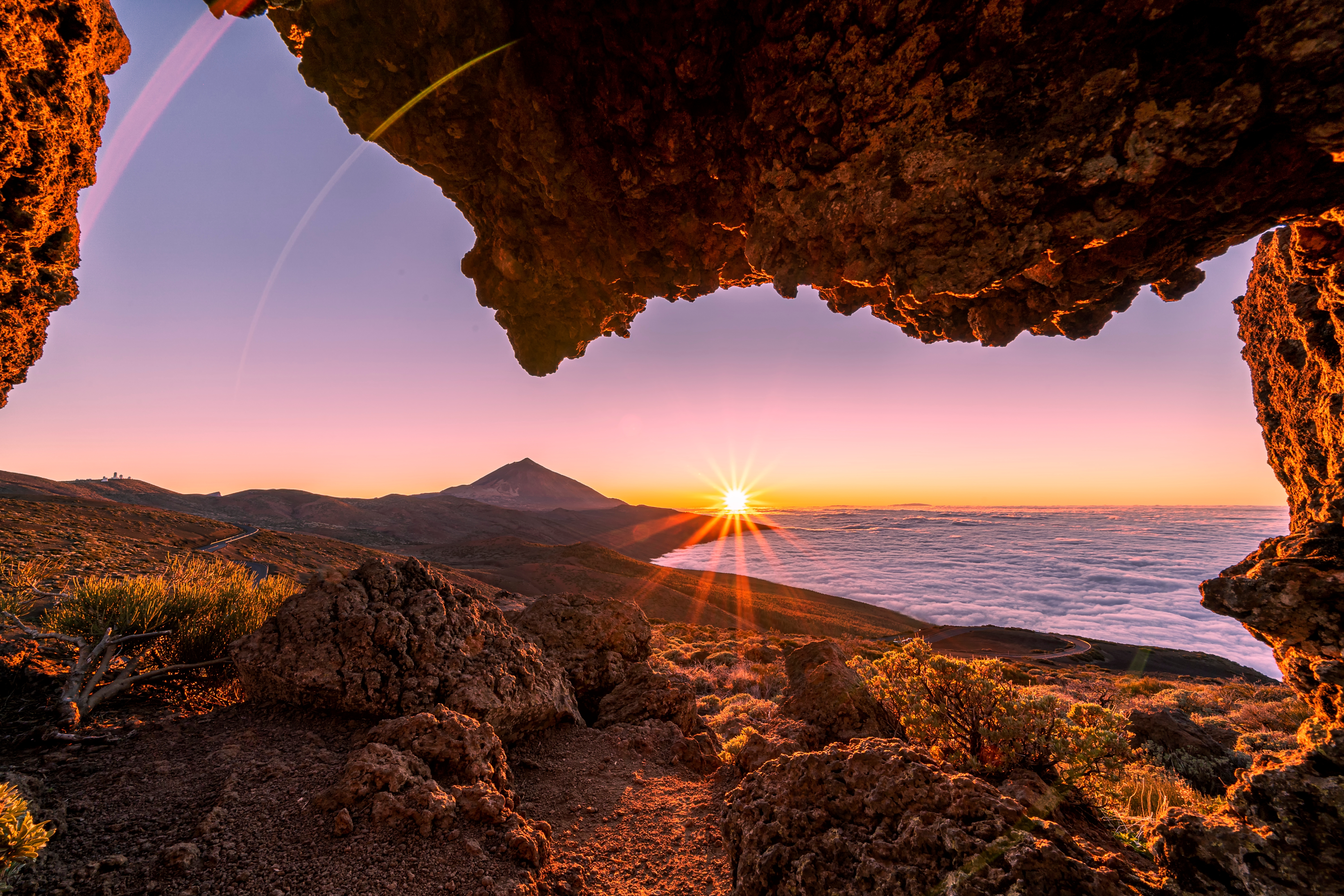 Gylden solopgang med udsigt over Teide vulkan og kyst fra klippehule på Tenerife