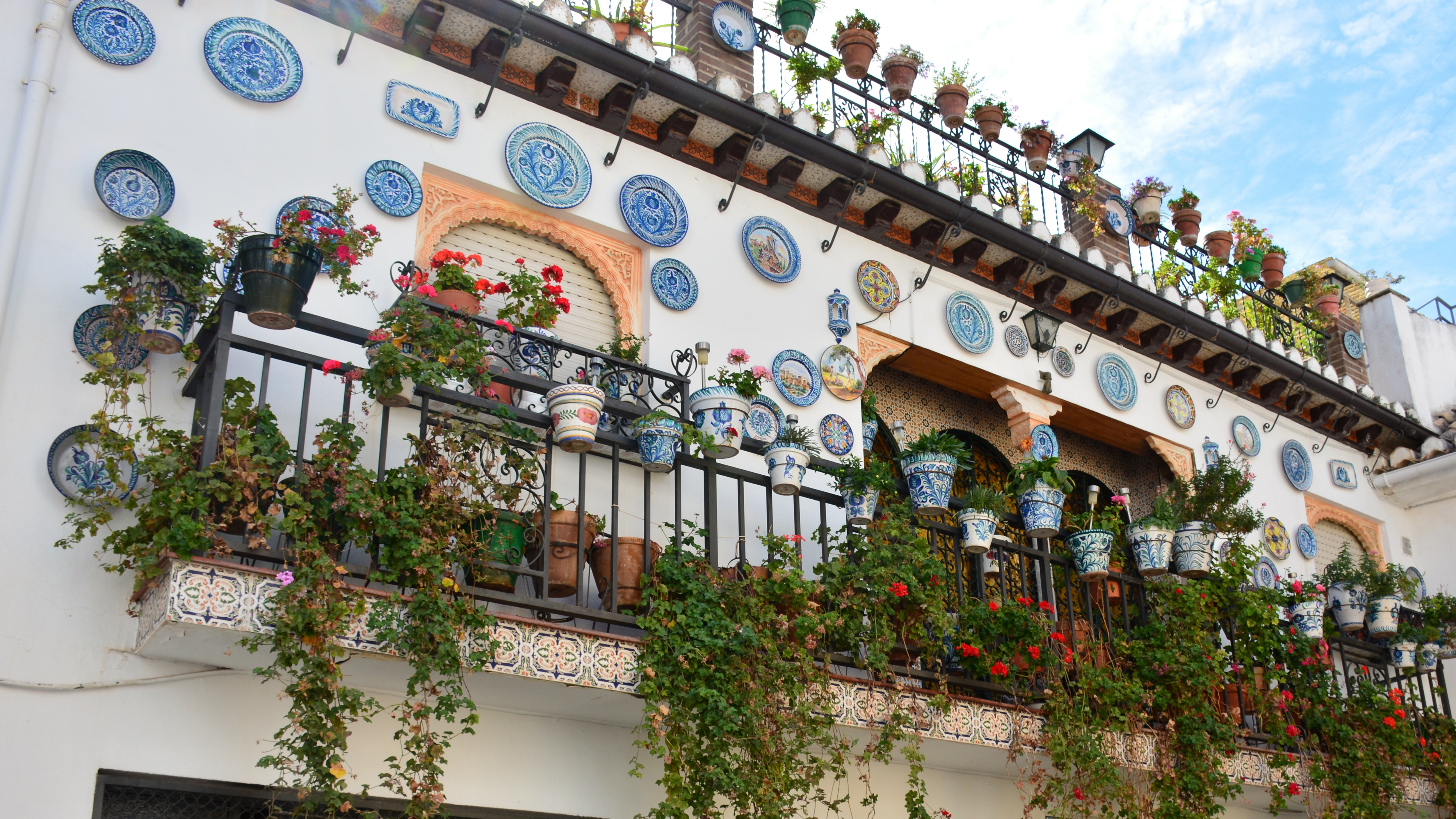 Farverig balkon i Mijas med traditionelle spanske keramikfade og blomsterpotter langs den hvide facade