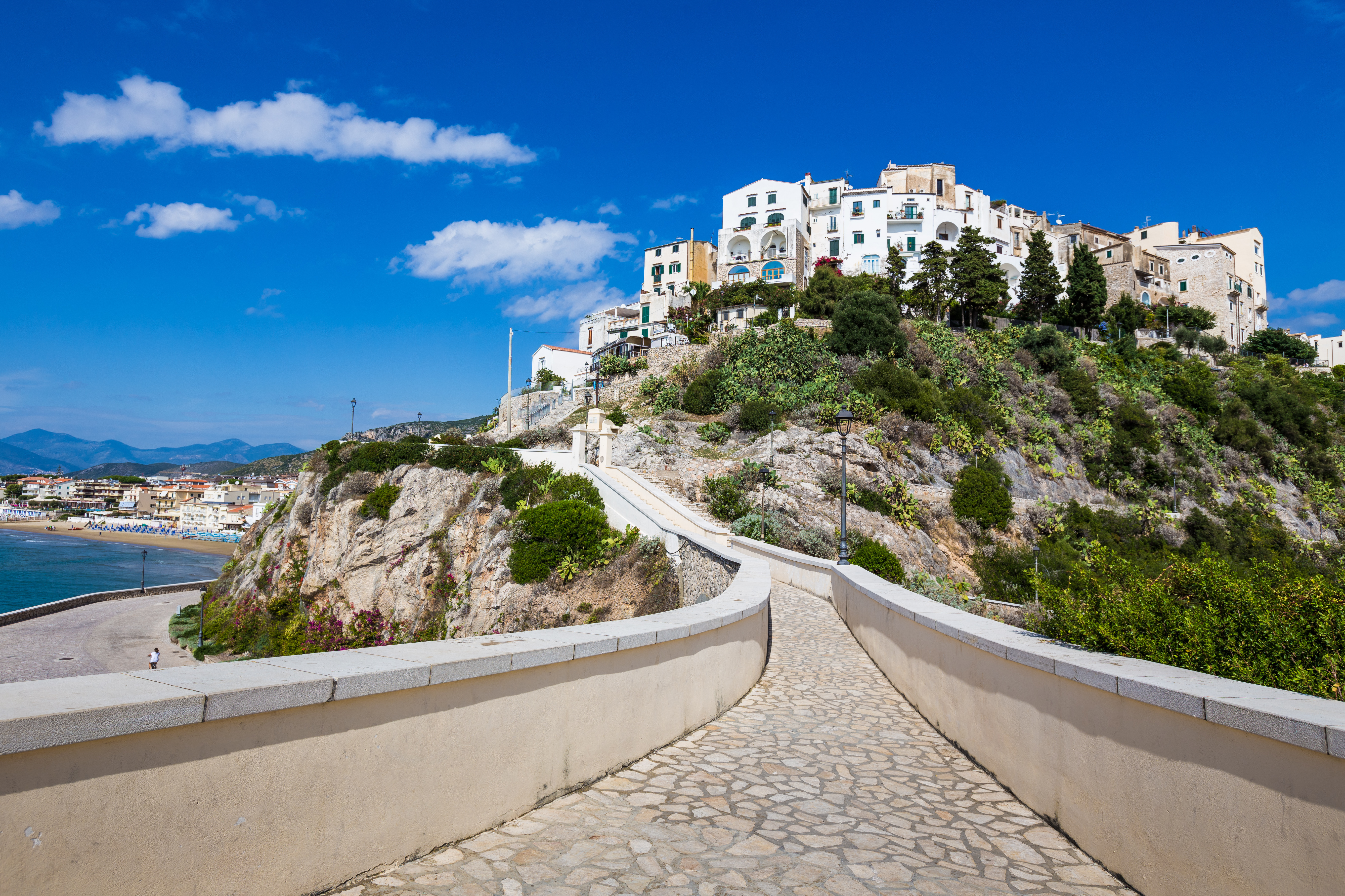 Idyllisk udsigt over Sperlongas hvide huse på klippetoppen i Lazio, Italien, med strandpromenade og blåt hav i baggrunden