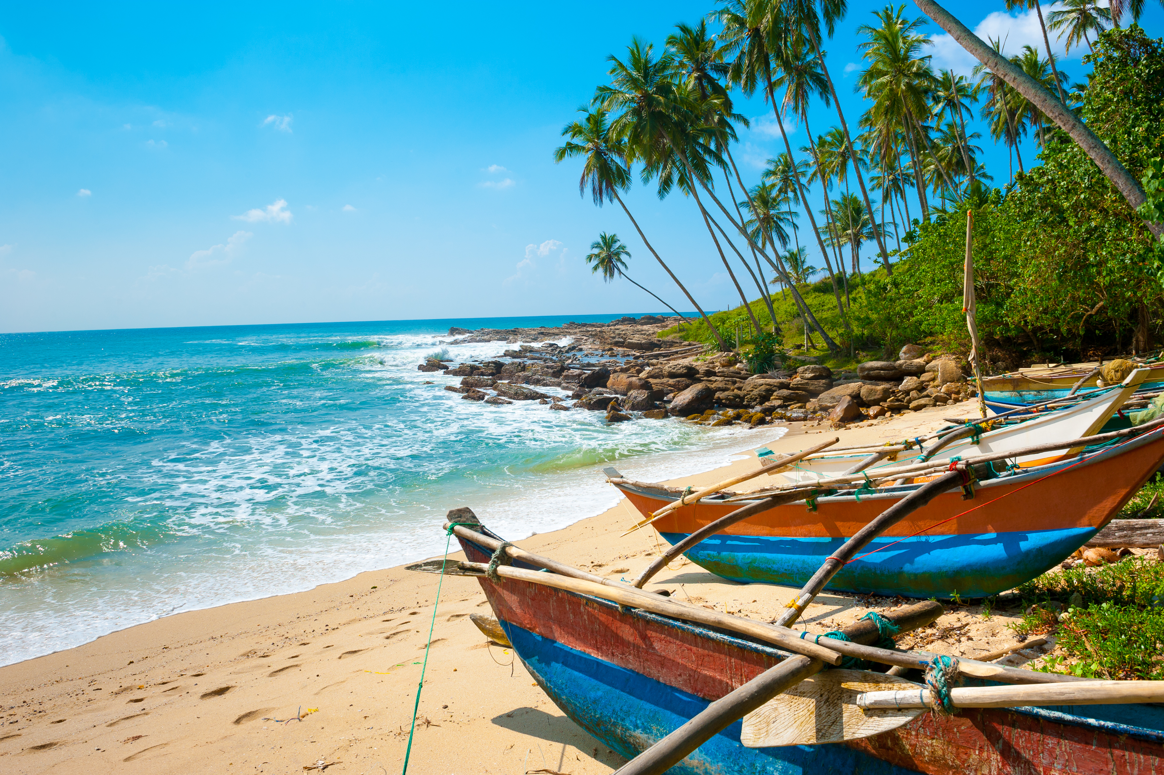Smuk uberørt strand ved Sri Lankas kyst med krystalklart turkisblåt vand, traditionelle fiskerbåde og skyggefulde palmer langs det hvide sand