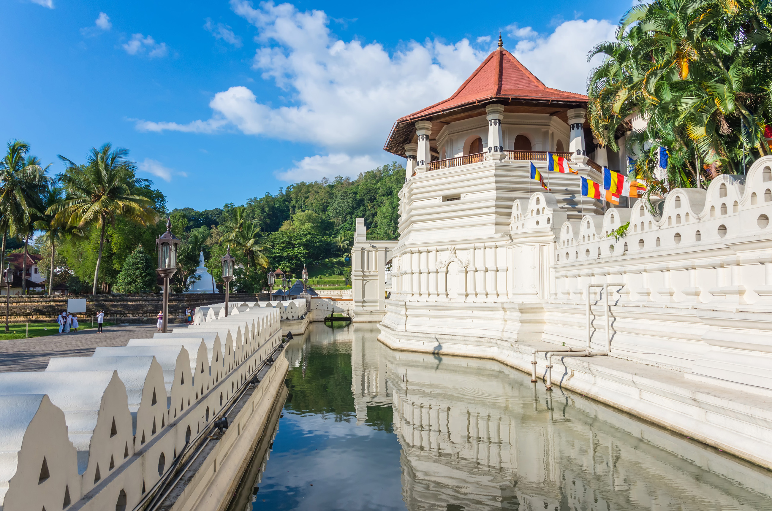 Det historiske Tempel for Tanden i Kandy, Sri Lanka, med imponerende hvide mure og rødt tag, omgivet af vandgrav og tropiske palmer