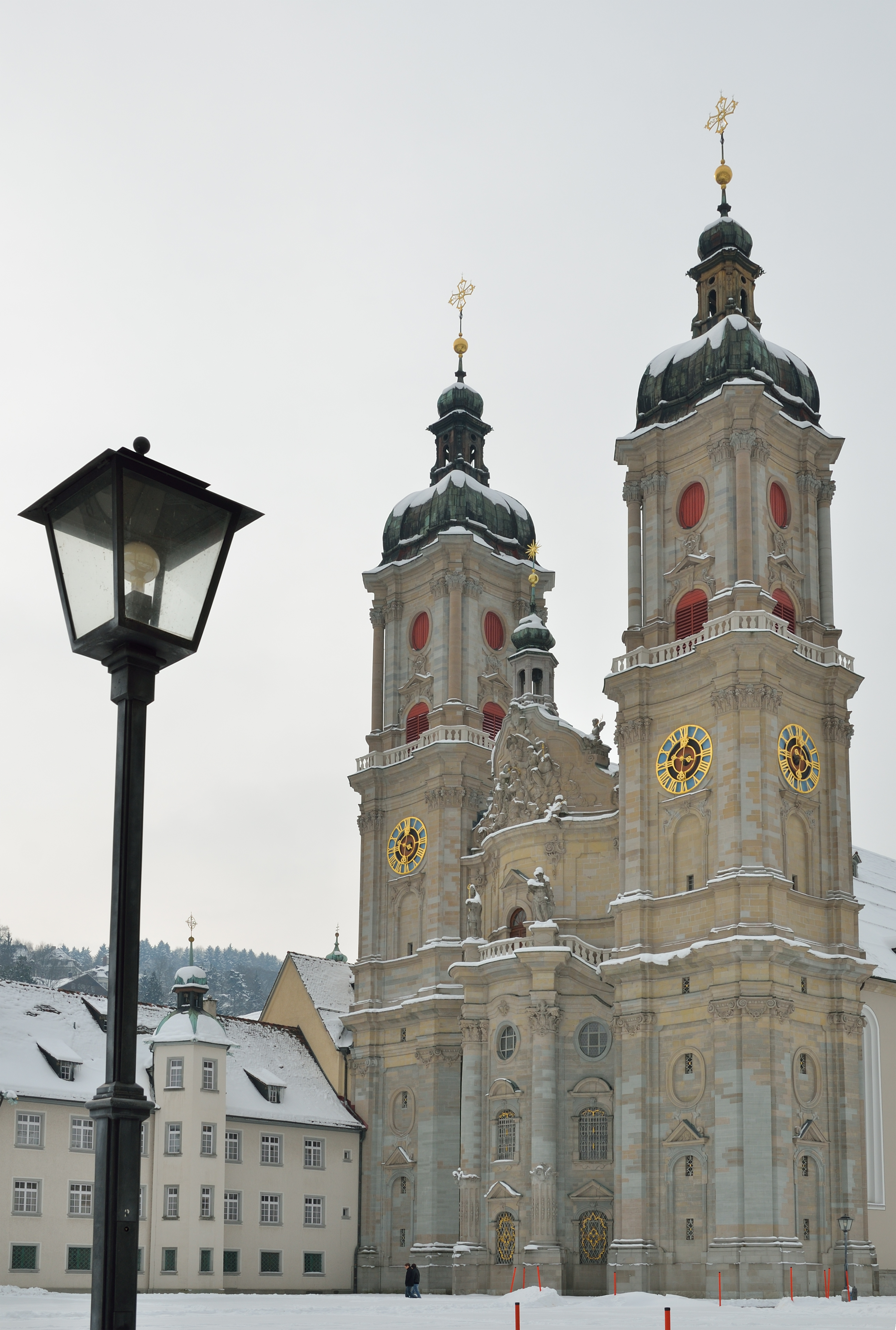 Imponerende barok domkirke i St. Gallen med to tårne prydet med gyldne kors og ure i snevejr i Schweiz