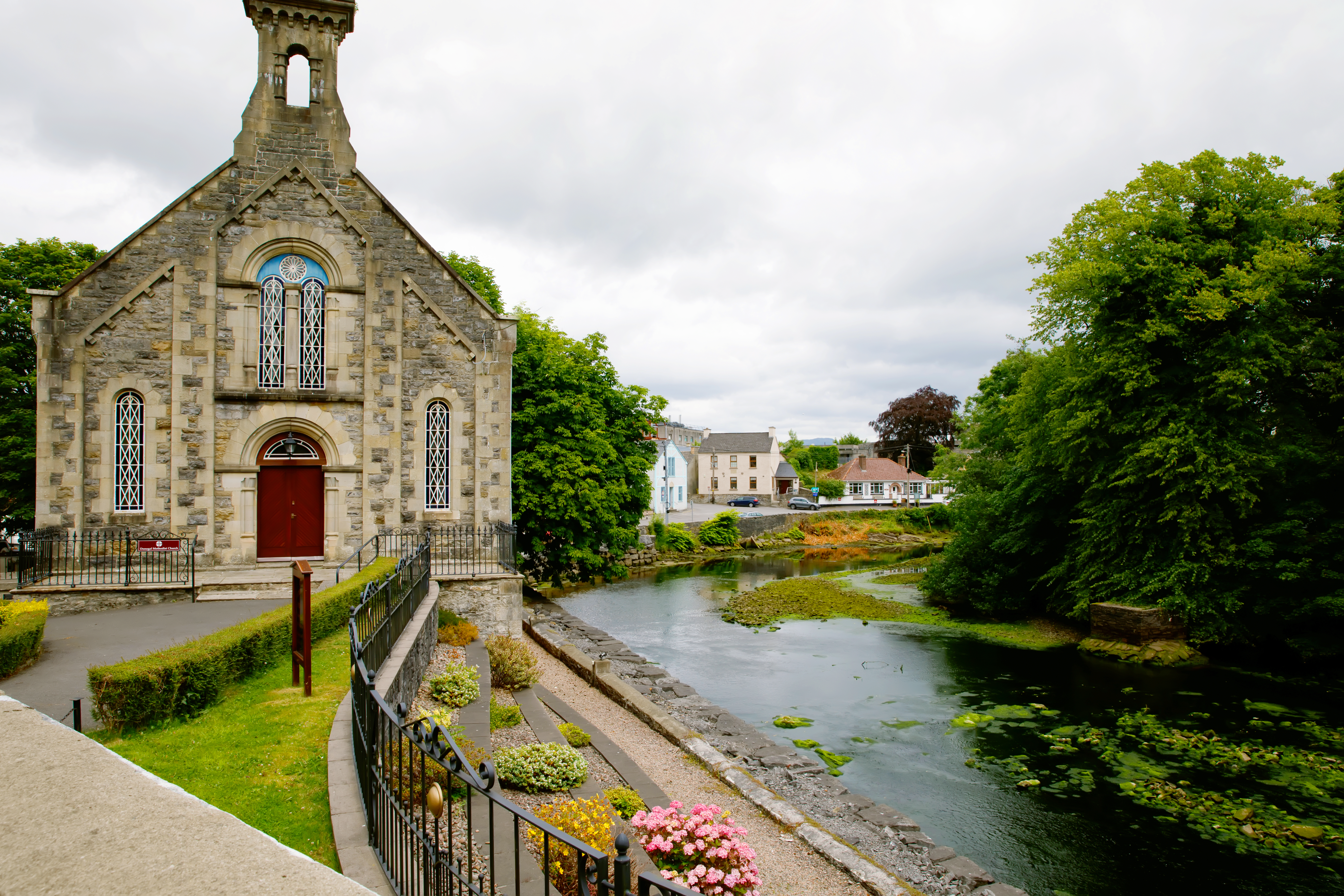 Historisk stenkirke ved en rolig flod i County Donegal, Irland, med smukke grønne omgivelser og blomster