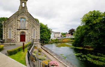 Historisk stenkirke ved en rolig flod i County Donegal, Irland, med smukke grønne omgivelser og blomster