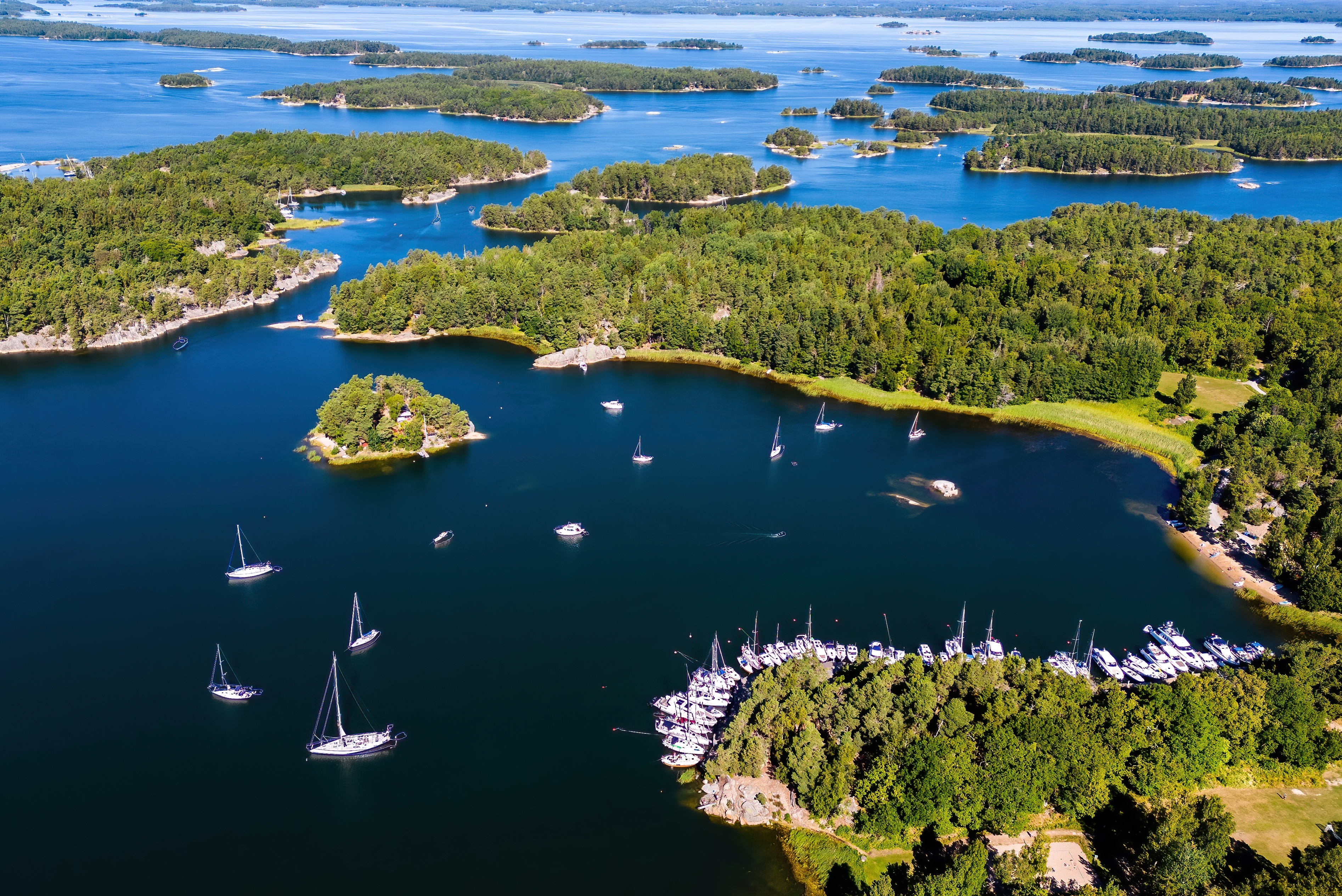 Luftfoto over Stockholms skærgård med sejlbåde ankret i rolig bugt og tæt skov på øerne