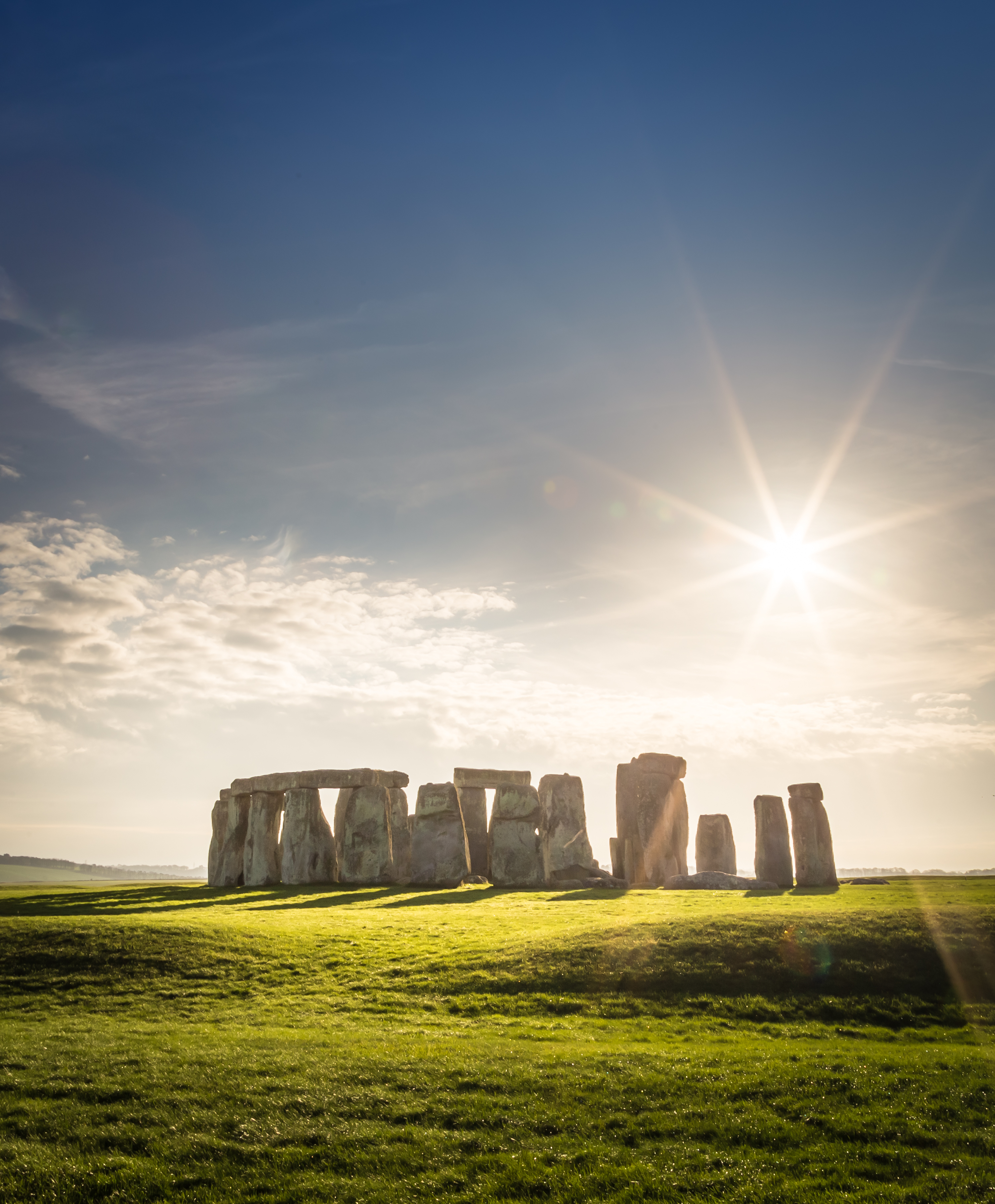 Det ikoniske Stonehenge stenmonment under blå himmel med solstråler i England