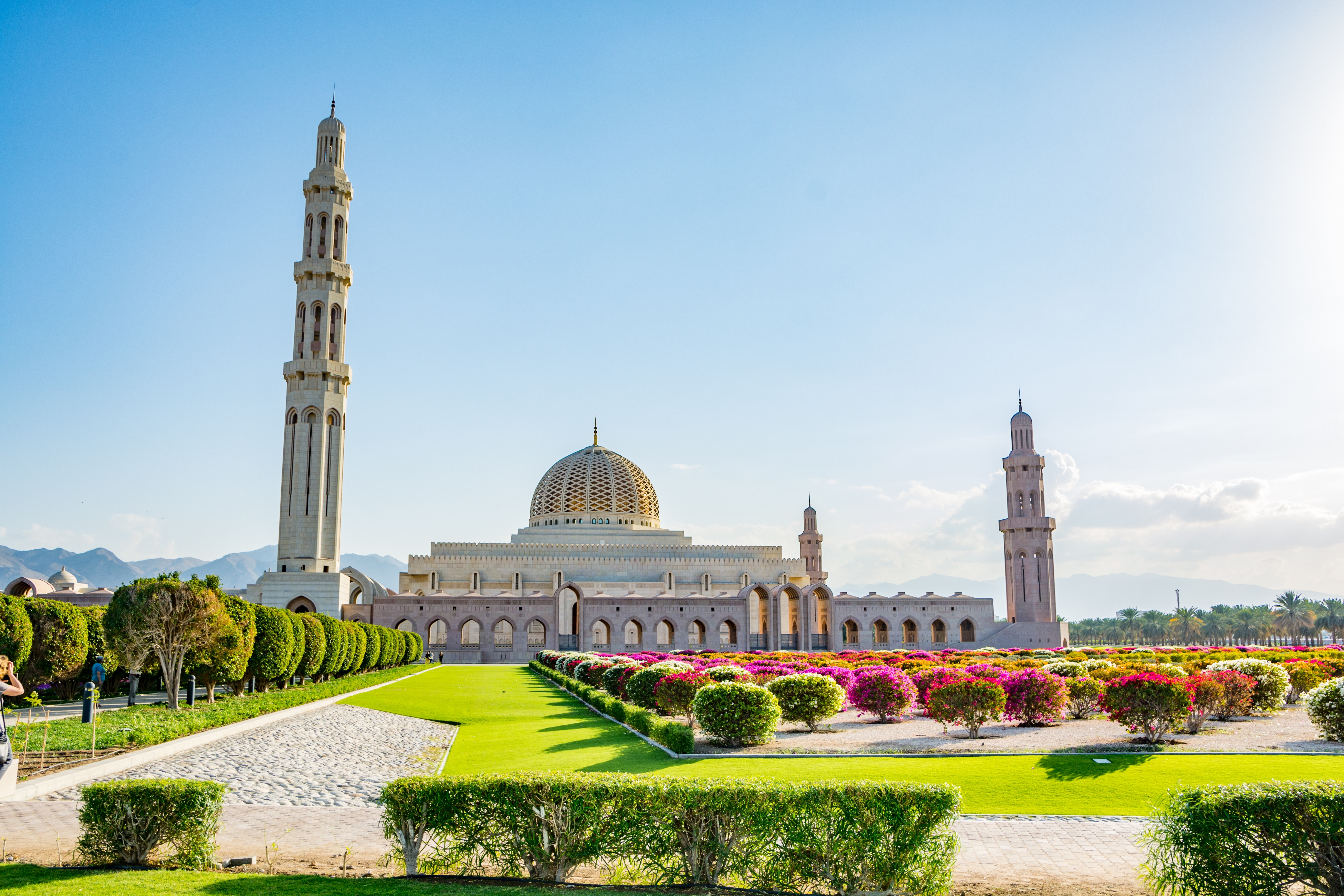 Sultan Qaboos Store Moske i Muscat, Oman, omgivet af farverige blomsterbede og grønne haver med klippede hække og høje minareter