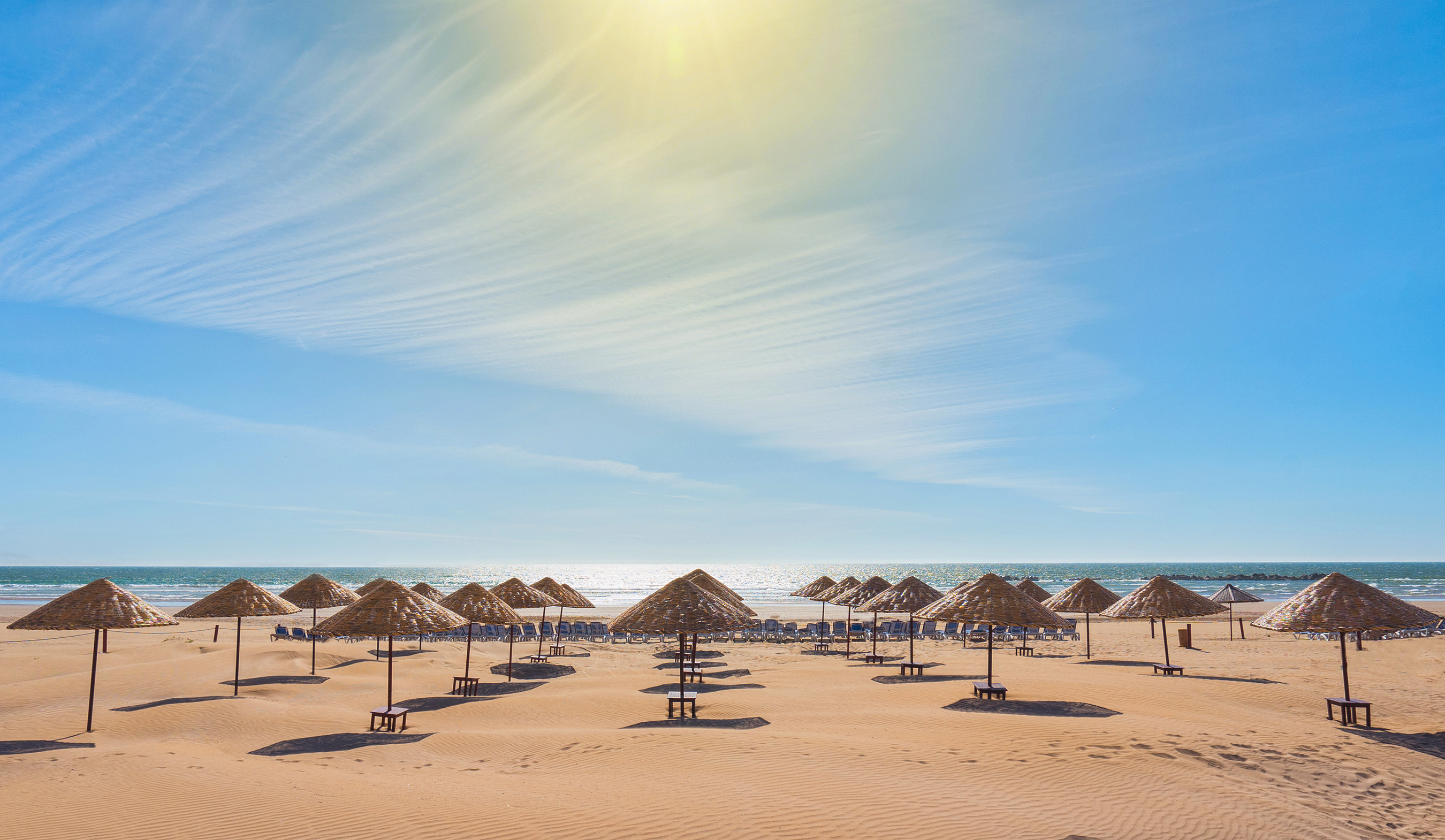 Fantastisk strandferie i Agadir med parasoller af strå og solstole på det varme sand under blå himmel