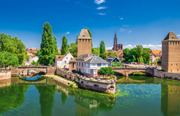 Malerisk udsigt over Strasbourgs gamle bro og tårne med farverige bindingsværkshuse under blå himmel
