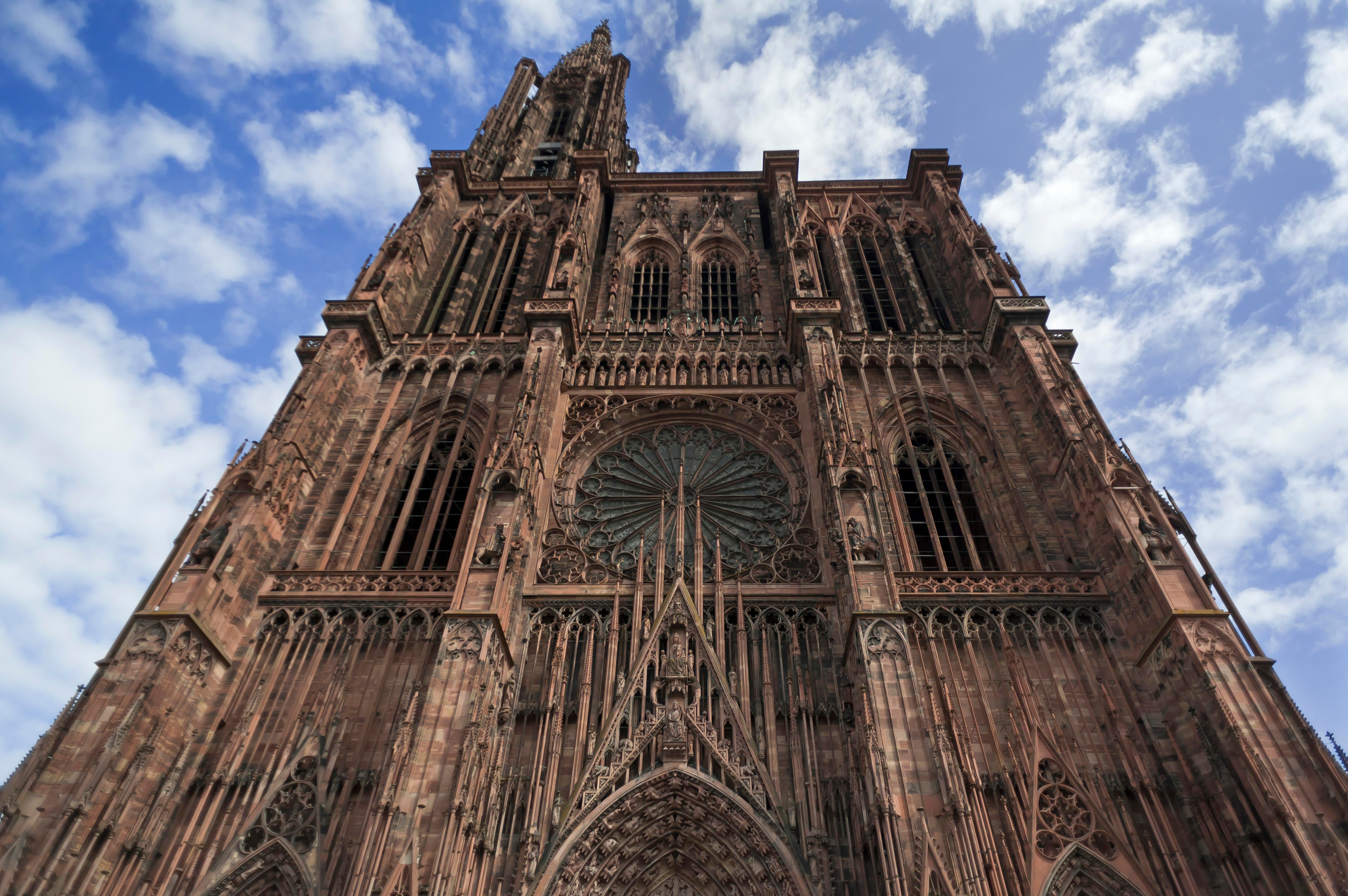 Spektakulær udsigt op ad den gotiske facade på Strasbourg Katedral i Alsace med detaljerede udskæringer og rosetvindue mod skyfyldt himmel
