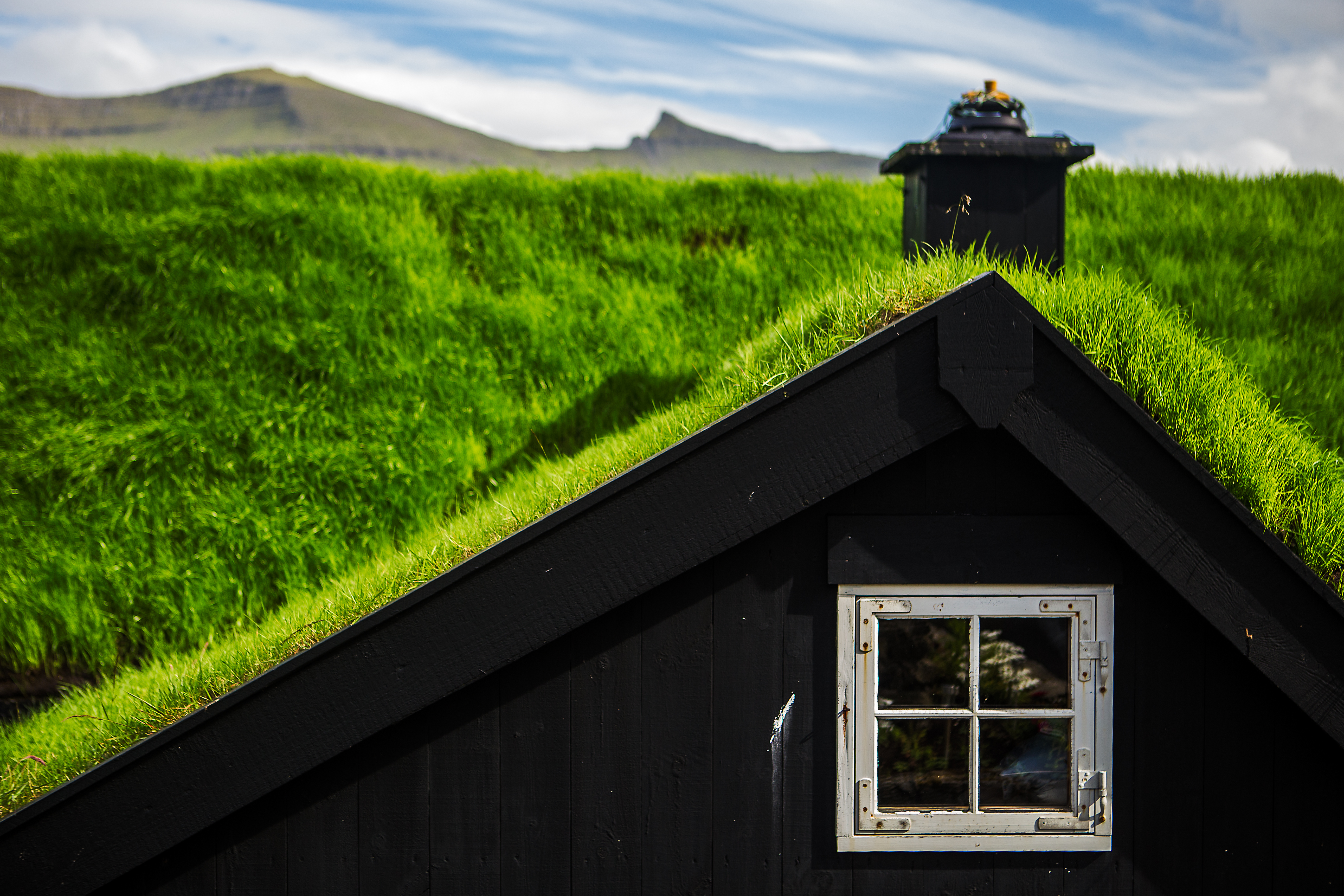 Malerisk sort træhus med traditionelt grønt tørvtag og hvidt vindue i den historiske bygd Kirkjubøur på Færøerne