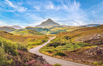 Grønne skotske højlande med snoet landevej mod Ben Stack bjergtop i Sutherland på en sommerdag