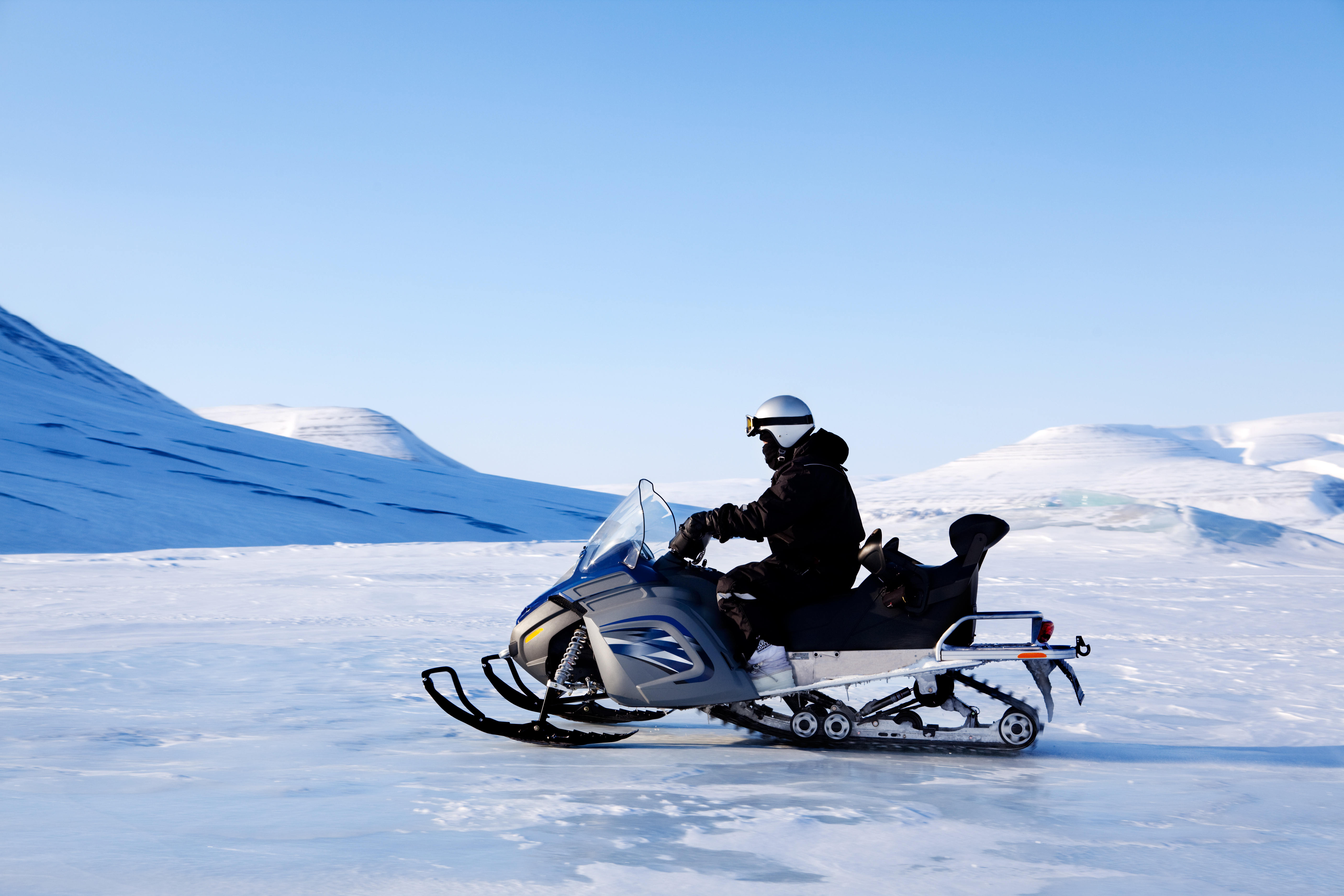 Spændende snowmobilekørsel på Svalbard i Arktis med storslåede snedækkede bjerge og blå vinterhimmel