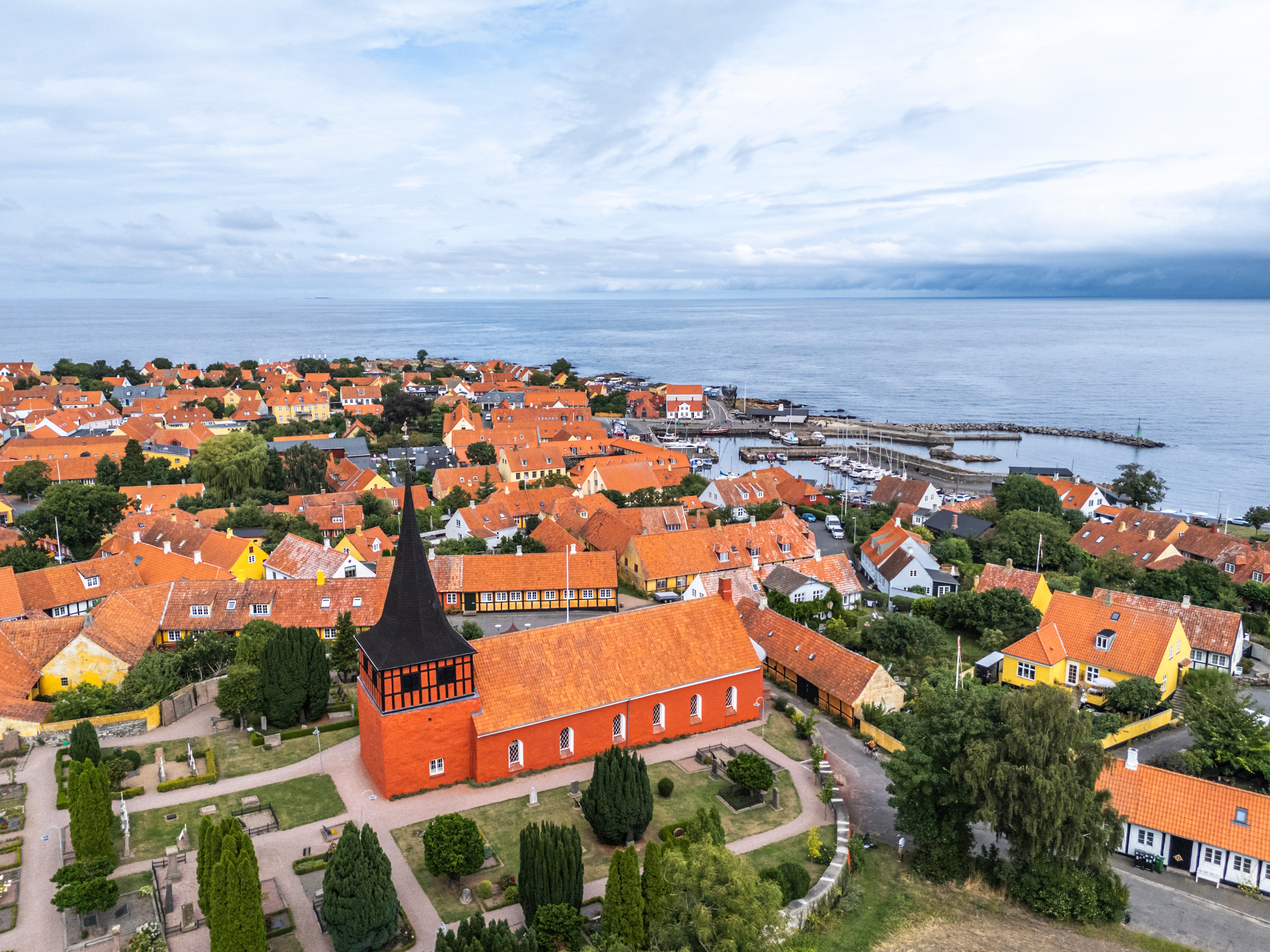 Fuglefoto over den idylliske by Svaneke på Bornholm med røde tage, historisk kirke og havn ved Østersøen