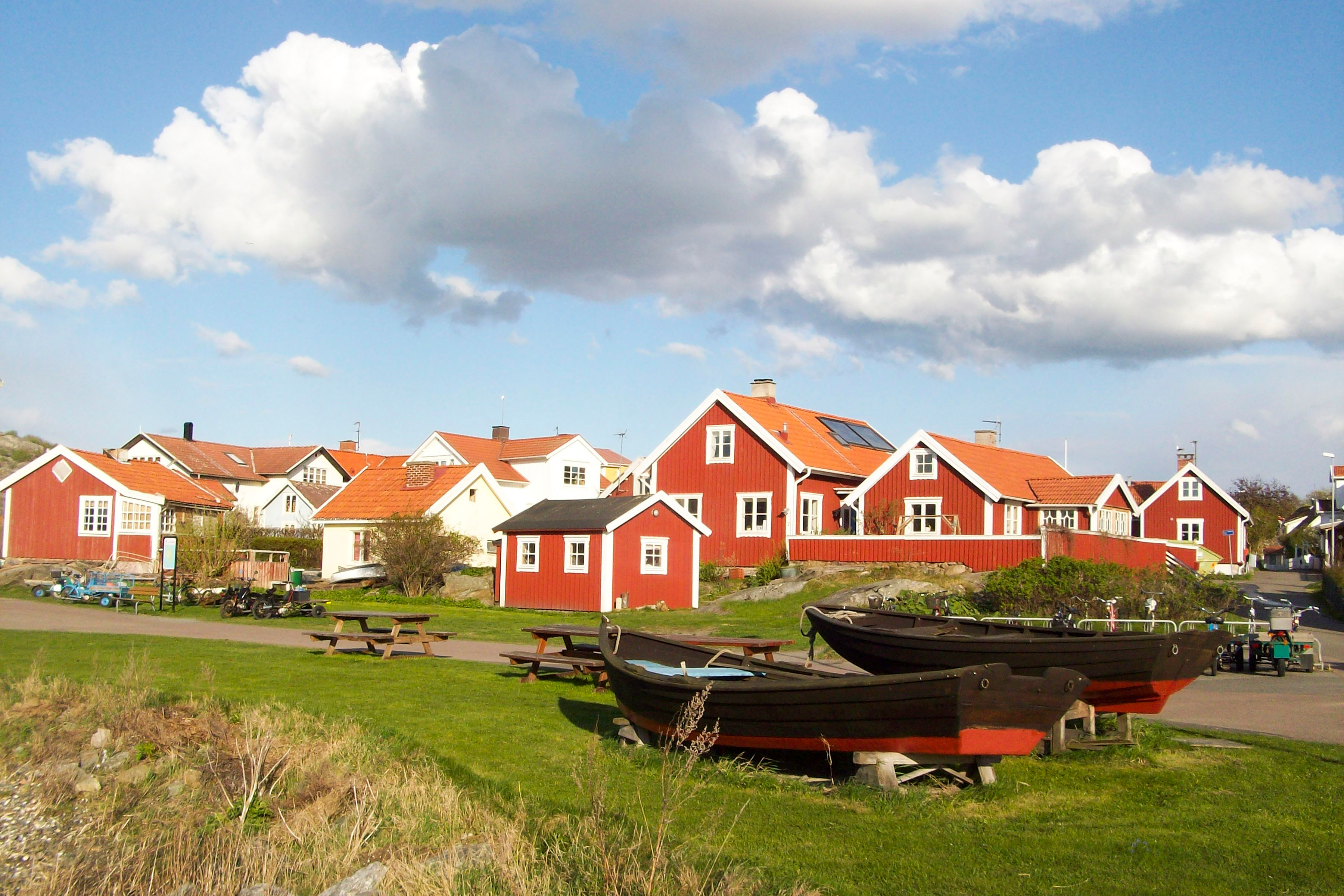 Hyggelig svensk landsby med røde Falun-huse og træbåde på grønt græs i smukt sommervejr