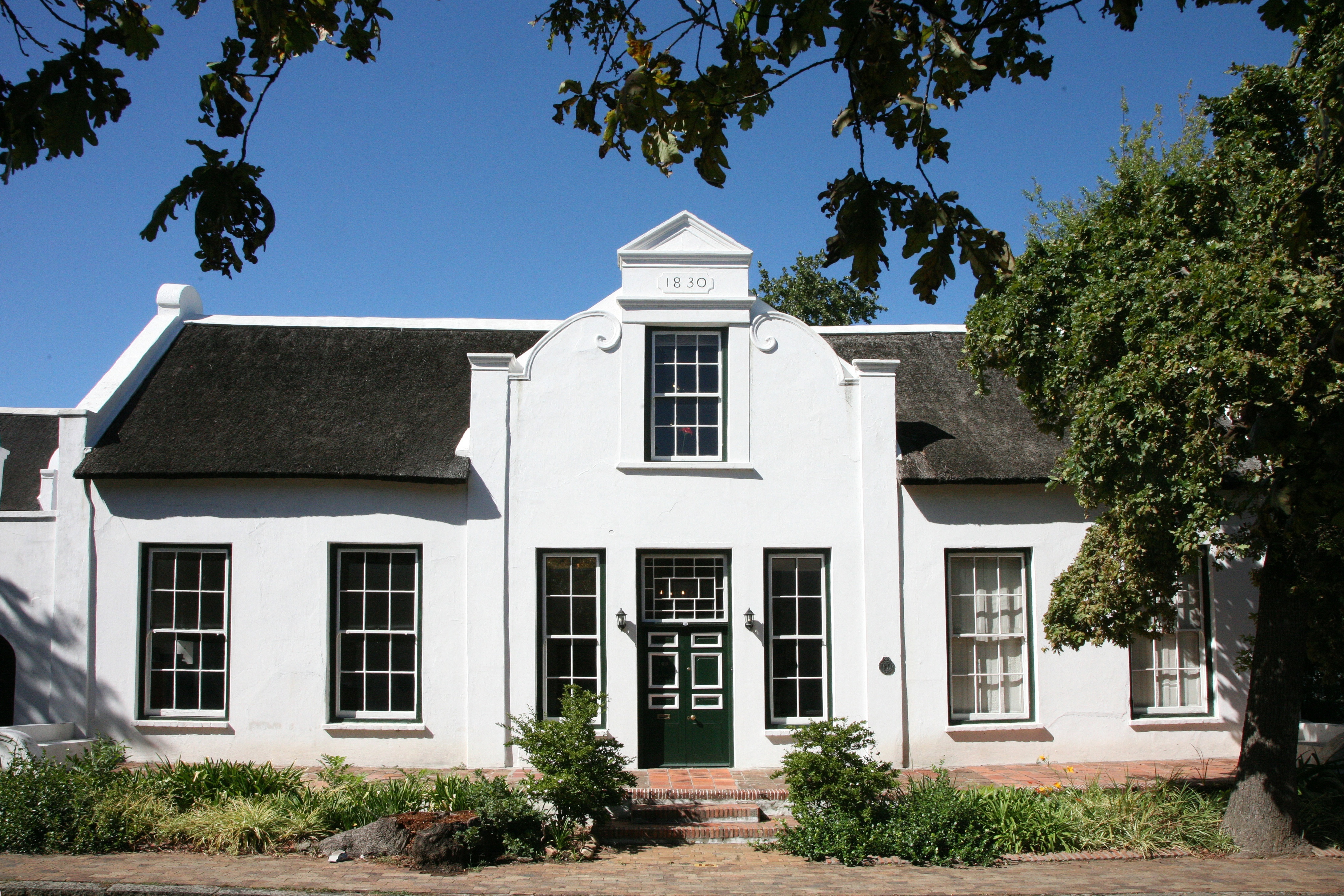 Charmerende Cape Dutch-arkitektur med hvidmalede mure og stråtag i Stellenbosch, Sydafrika