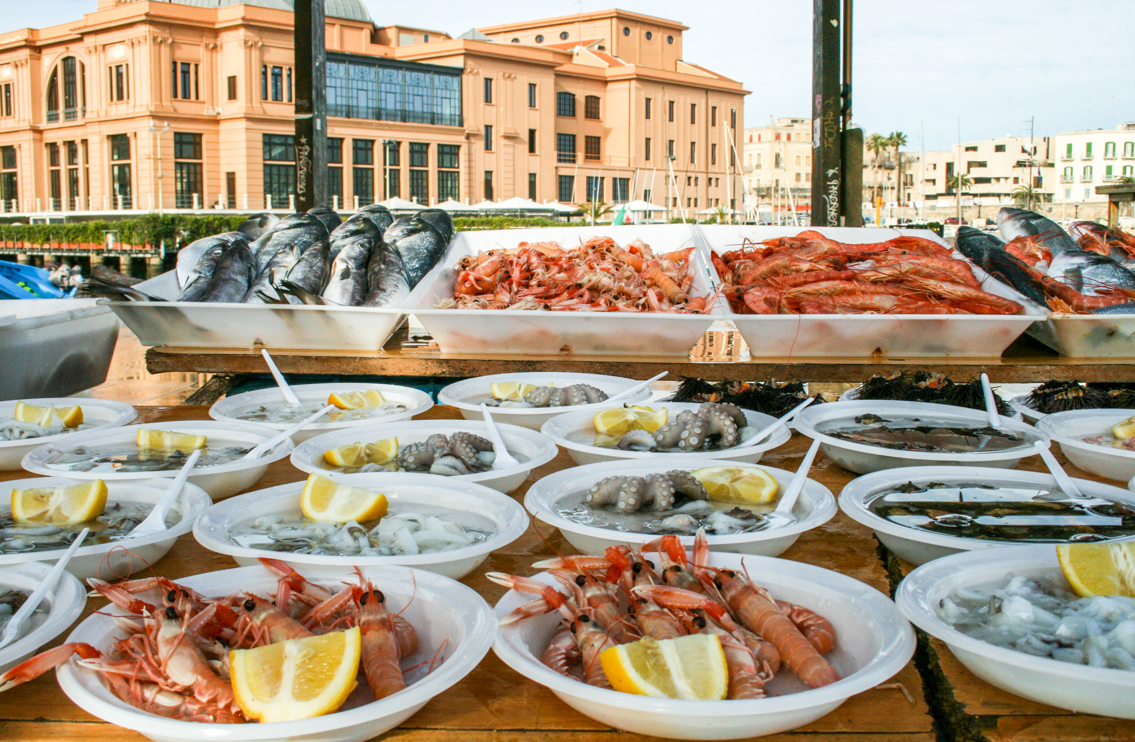 Farverigt udendørs fiskemarked i Bari, hvor lokale sælgere præsenterer dagens fangst af friske havfrugter og fisk på is med citron, en unik kulinarisk oplevelse i Syditaliens Apulien-region