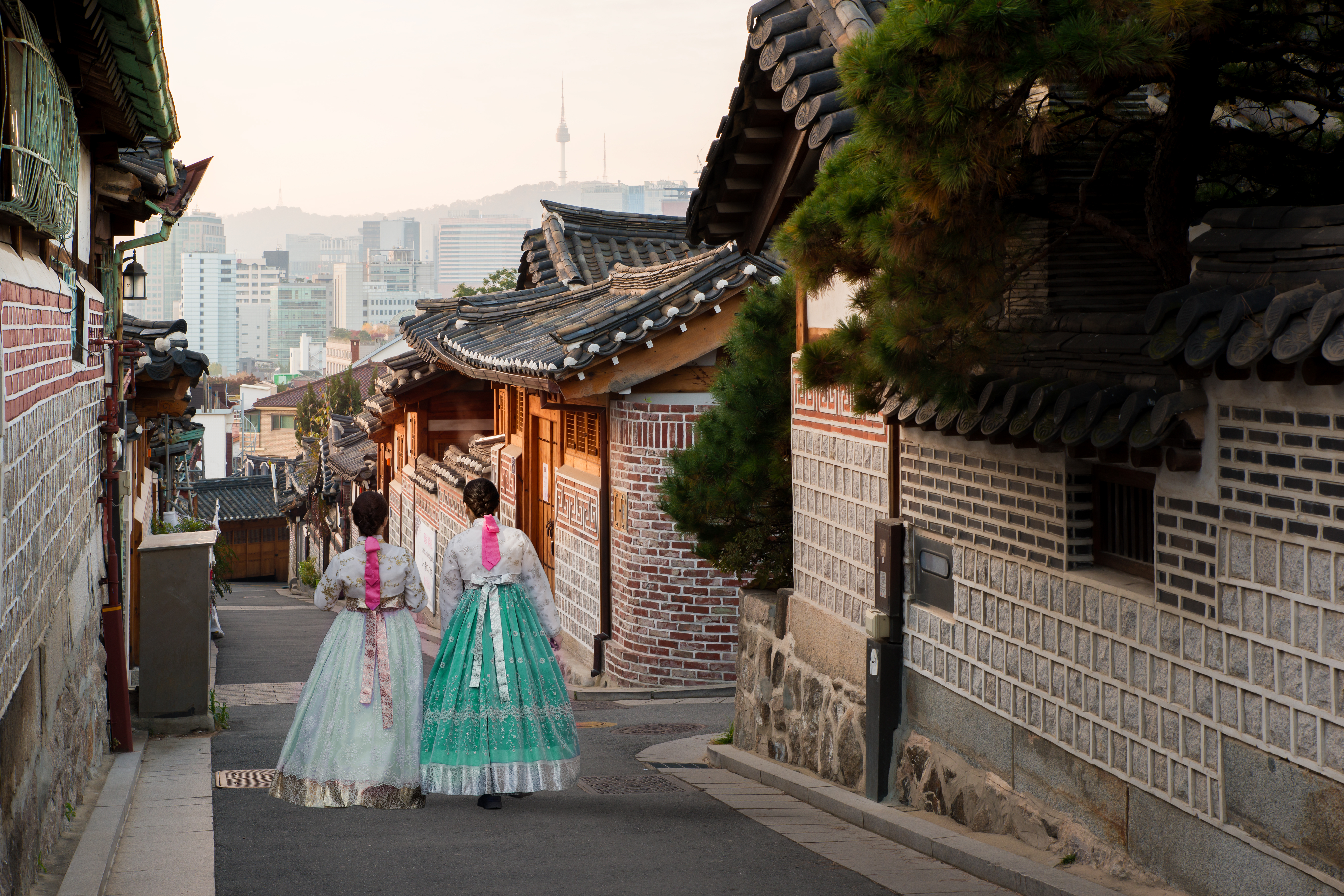 Malerisk scene fra Bukchon Hanok-landsbyen i Seoul, Sydkorea, hvor to kvinder i farvestrålende traditionelle hanbok-kjoler vandrer gennem de smukke historiske kvarterer