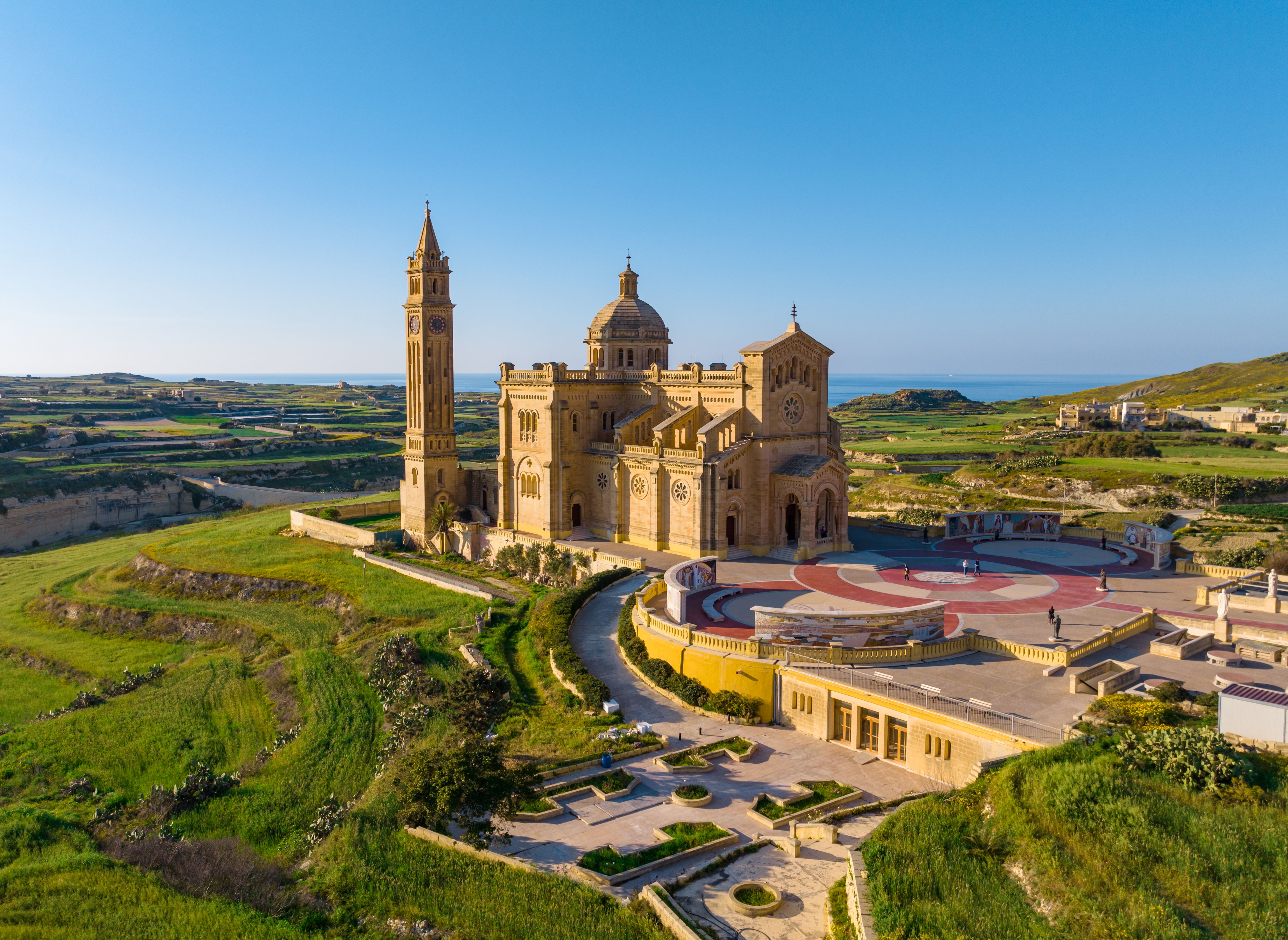 Ta' Pinu helligdommen på Gozo, Malta - en majestætisk basilika med klokketårn omgivet af grønne marker og Middelhavets azurblå vand