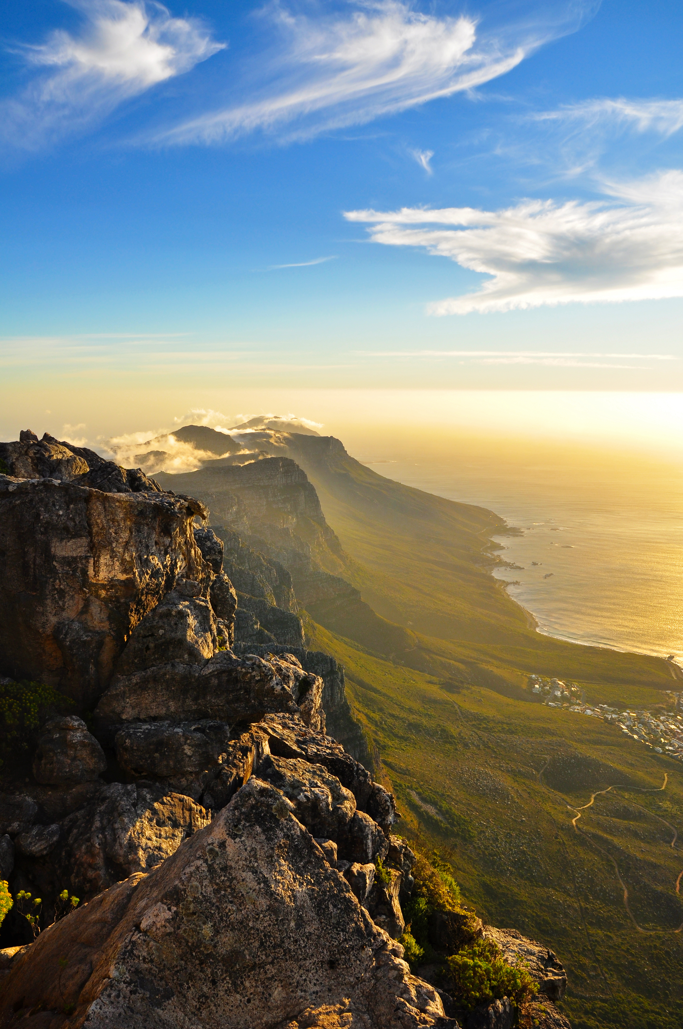 Storslået solnedgangsview fra Table Mountain med klipper i forgrunden og De Tolv Apostle langs Atlanterhavskysten i Cape Town