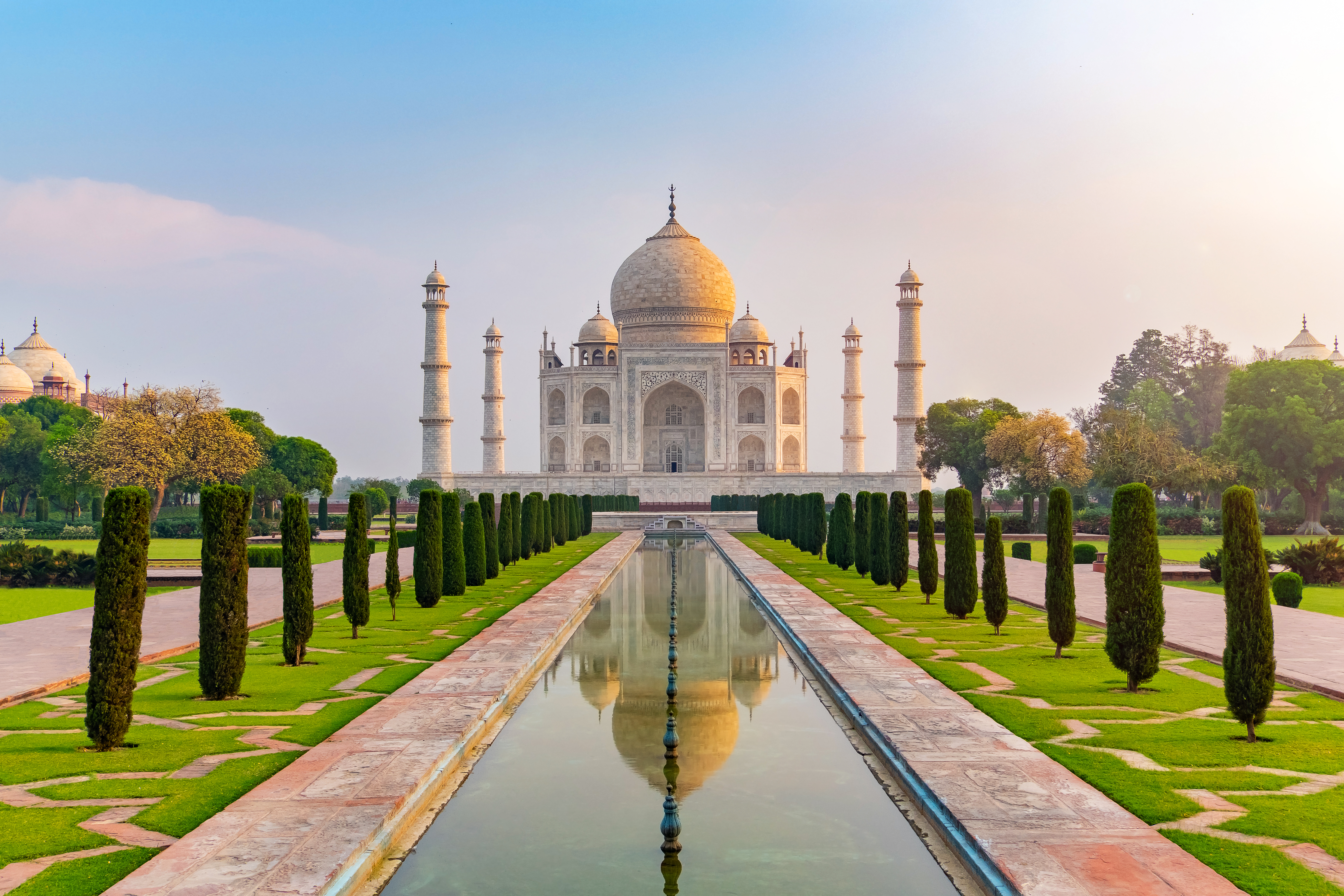 Taj Mahal mausoleet i Agra, Indien, omgivet af grønne haver og spejlet i vandbassin ved solopgang