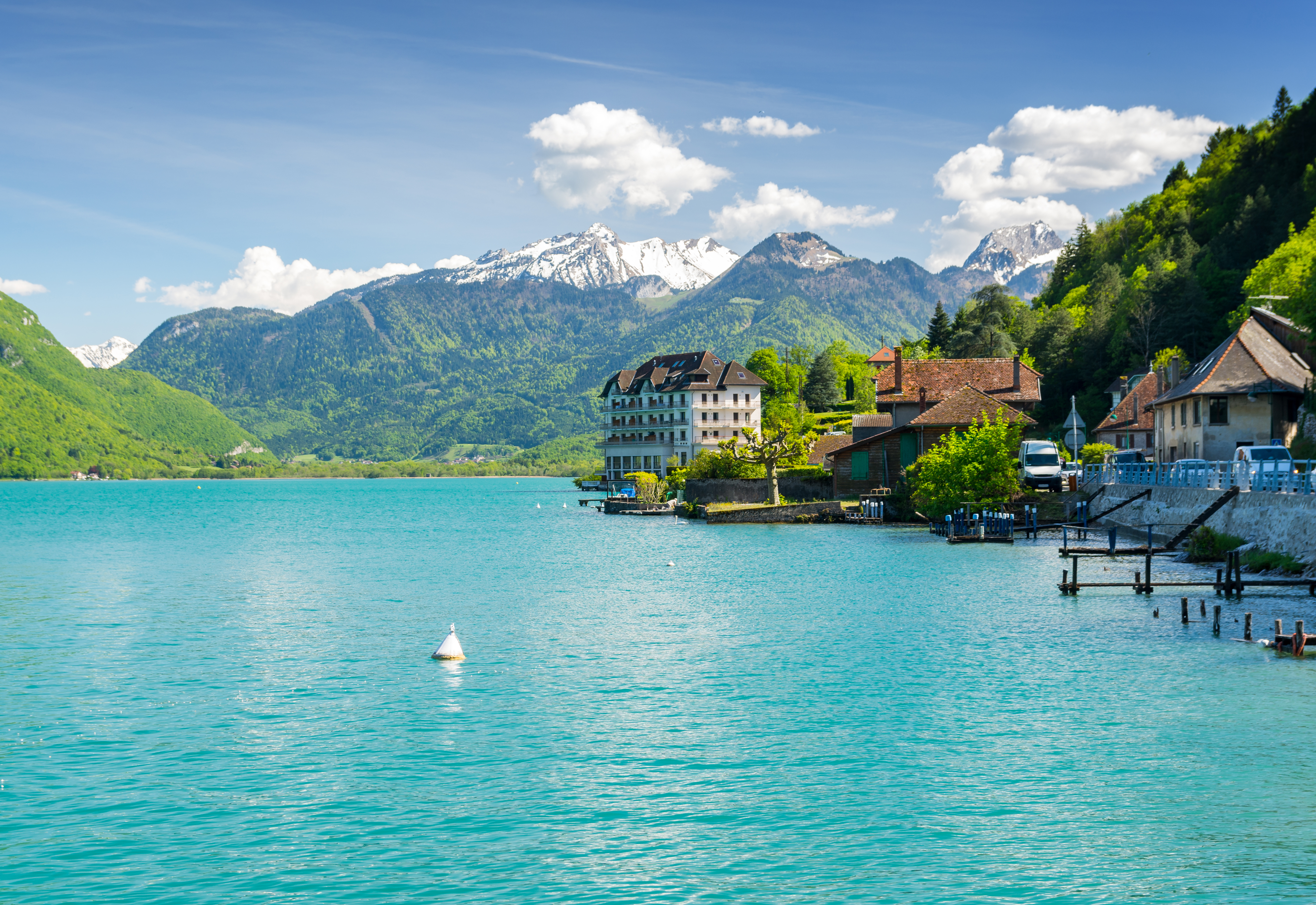 Pittoresk alpine landsby ved Annecy-søen med traditionelle huse og dramatiske bjerge baggrund