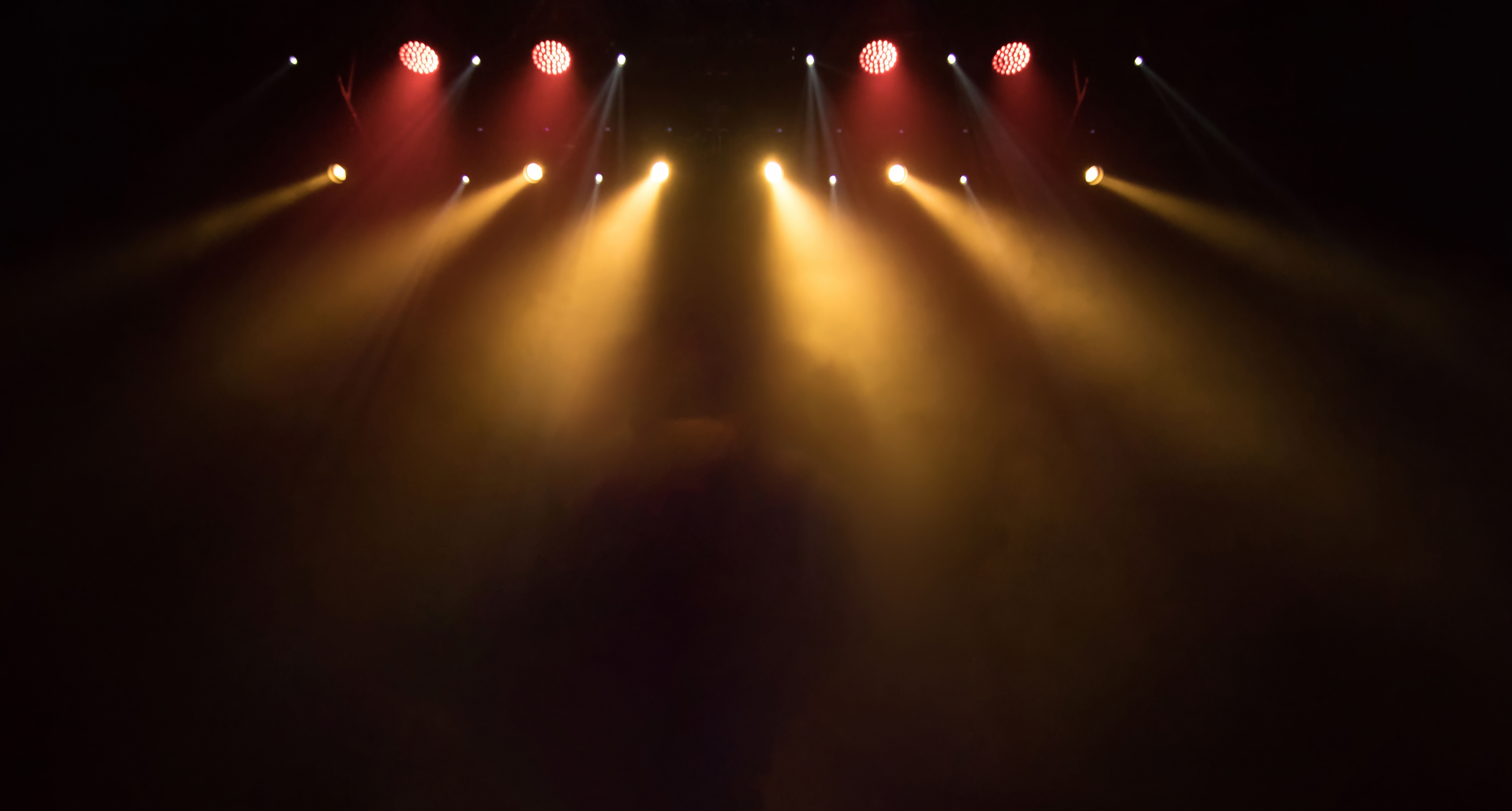 Flotte gyldne scenespotlights der lyser gennem røg på en teater- eller koncertscene – perfekt til rejseoplevelser