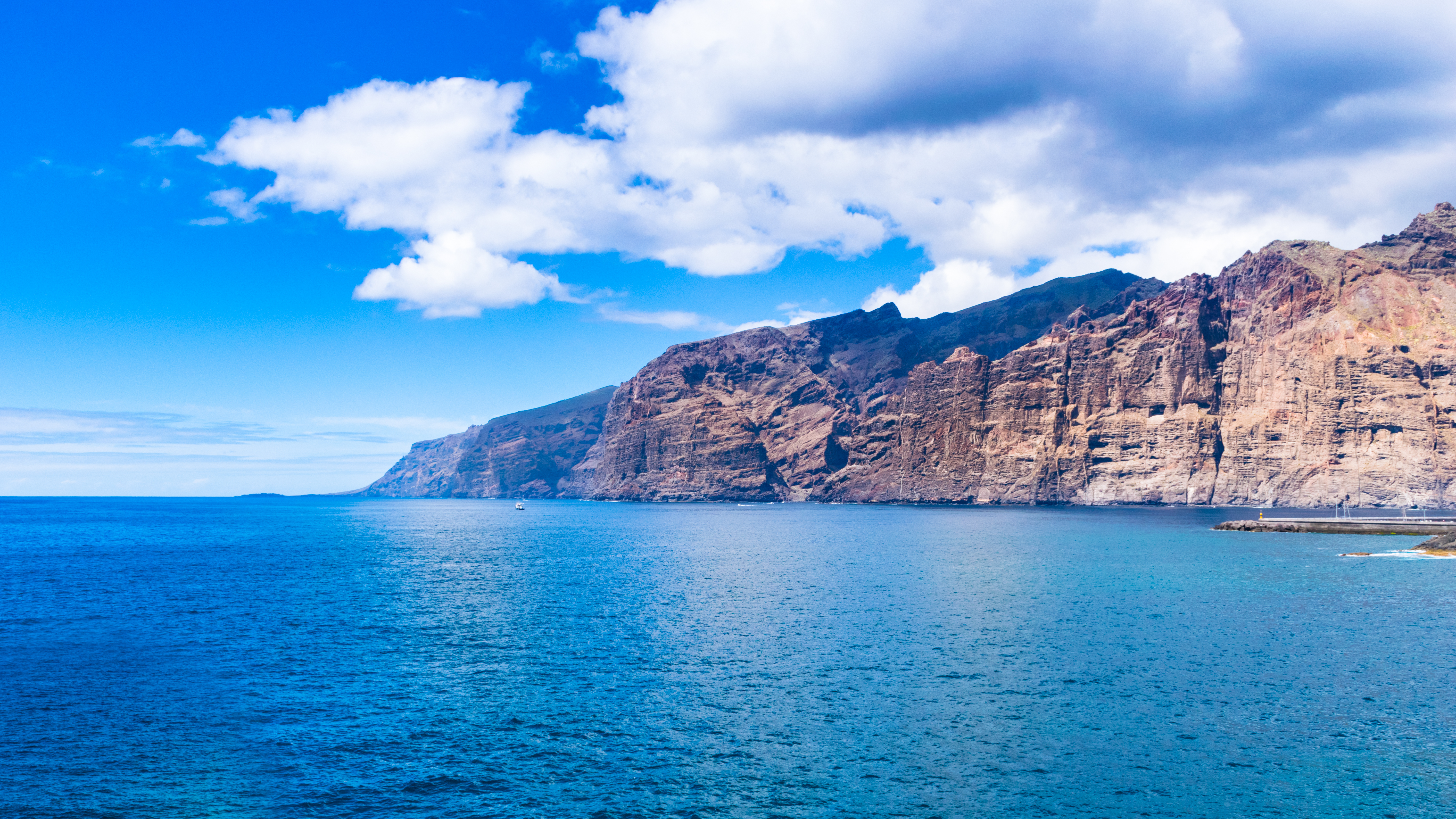 Majestætiske klipper ved Tenerife kyst med turkisblåt ocean og hvide skyer