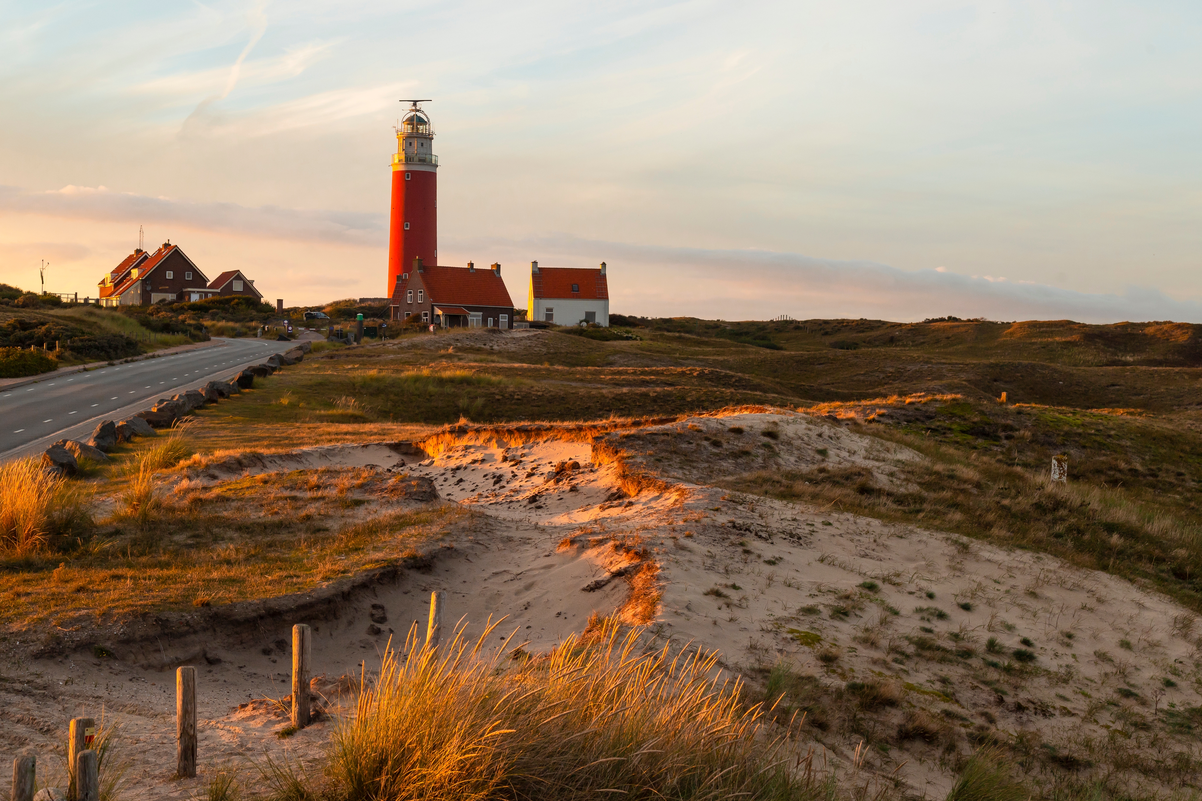 Smukt rødt fyrtårn på Texel øen i Nederlandene fotograferet ved solnedgang med sandklitter og græs i det bølgende kystlandskab