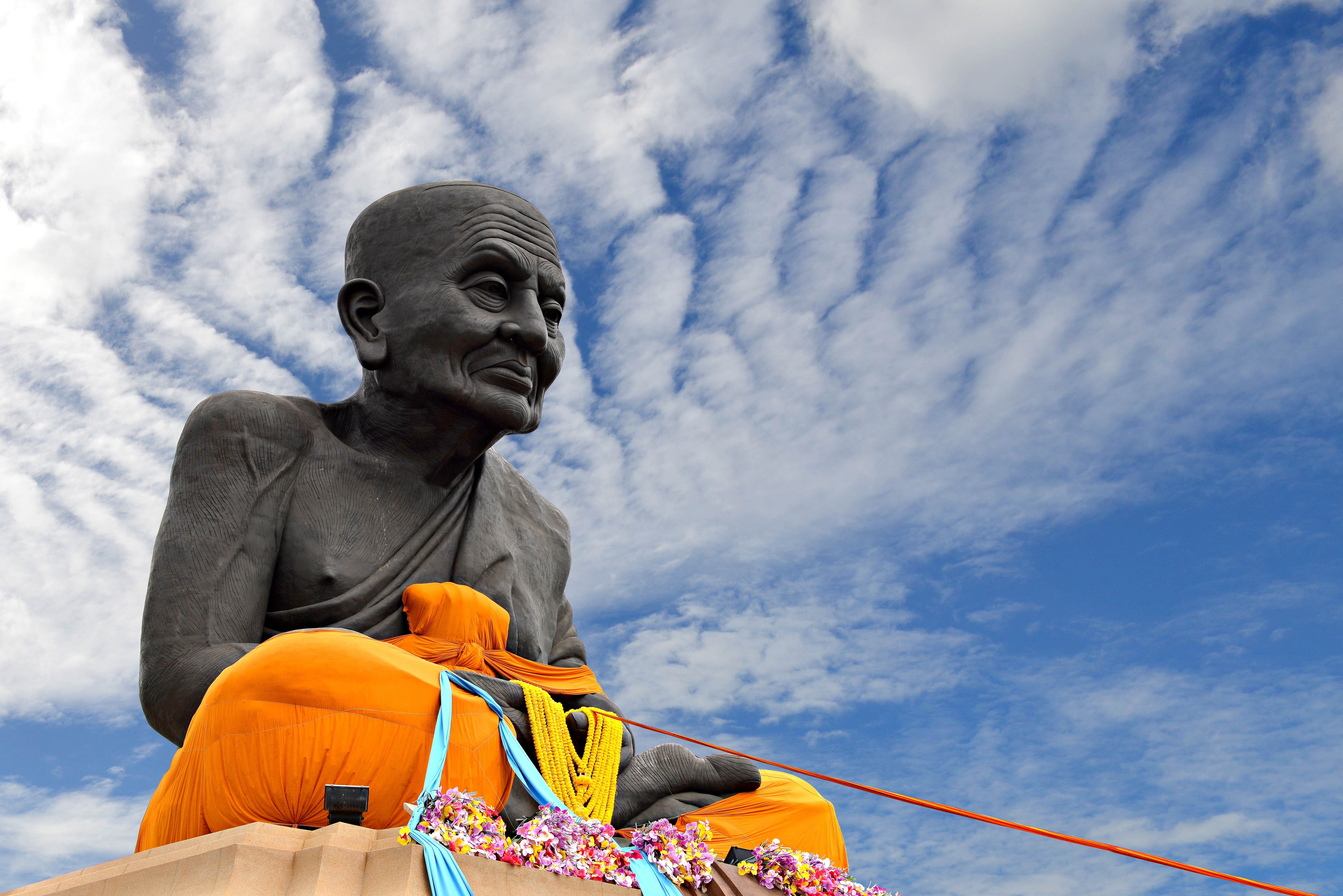 Imponerende buddhist mønke statue i orange under thailandsk himmel