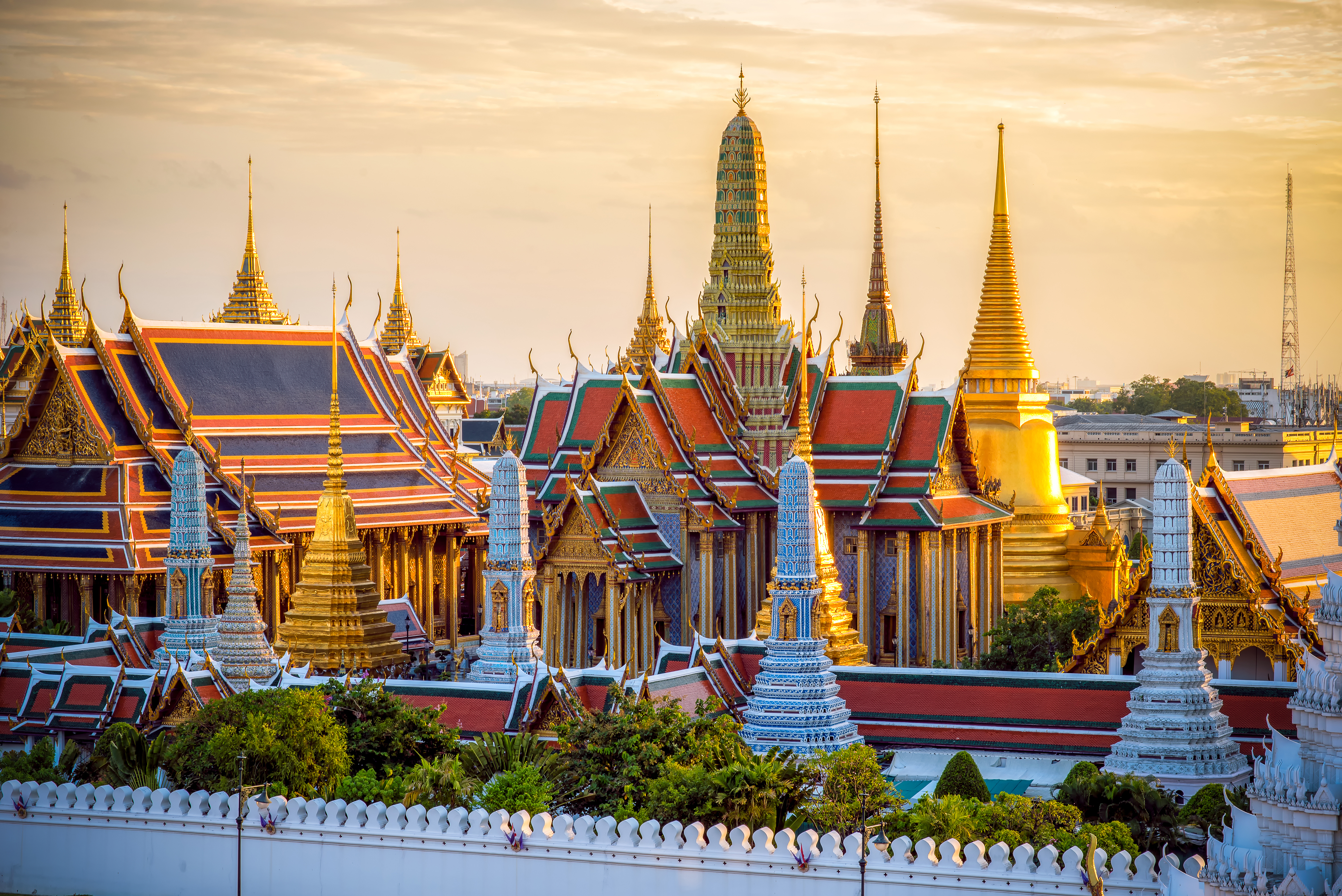 Storslået udsigt over det historiske Grand Palace og Wat Phra Kaew tempelkompleks i Bangkok, Thailand, med den dramatiske solnedgangshimmel som baggrund